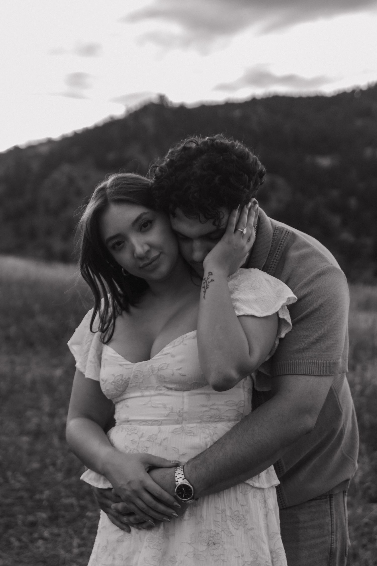 Black and white portrait of couple embracing intimately with mountain landscape in background.
