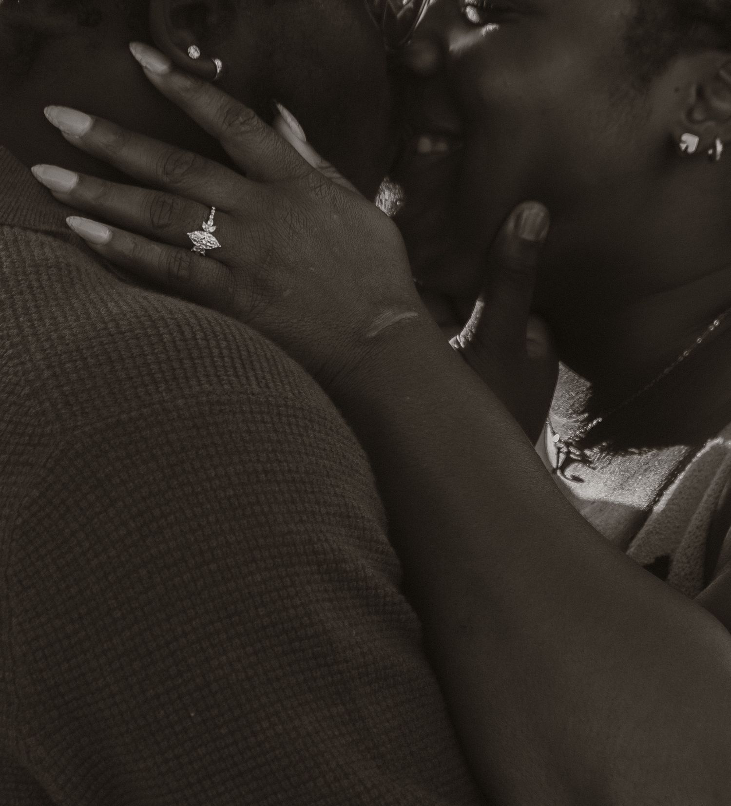 A black and white close-up photo showing hands with rings in an intimate embrace.