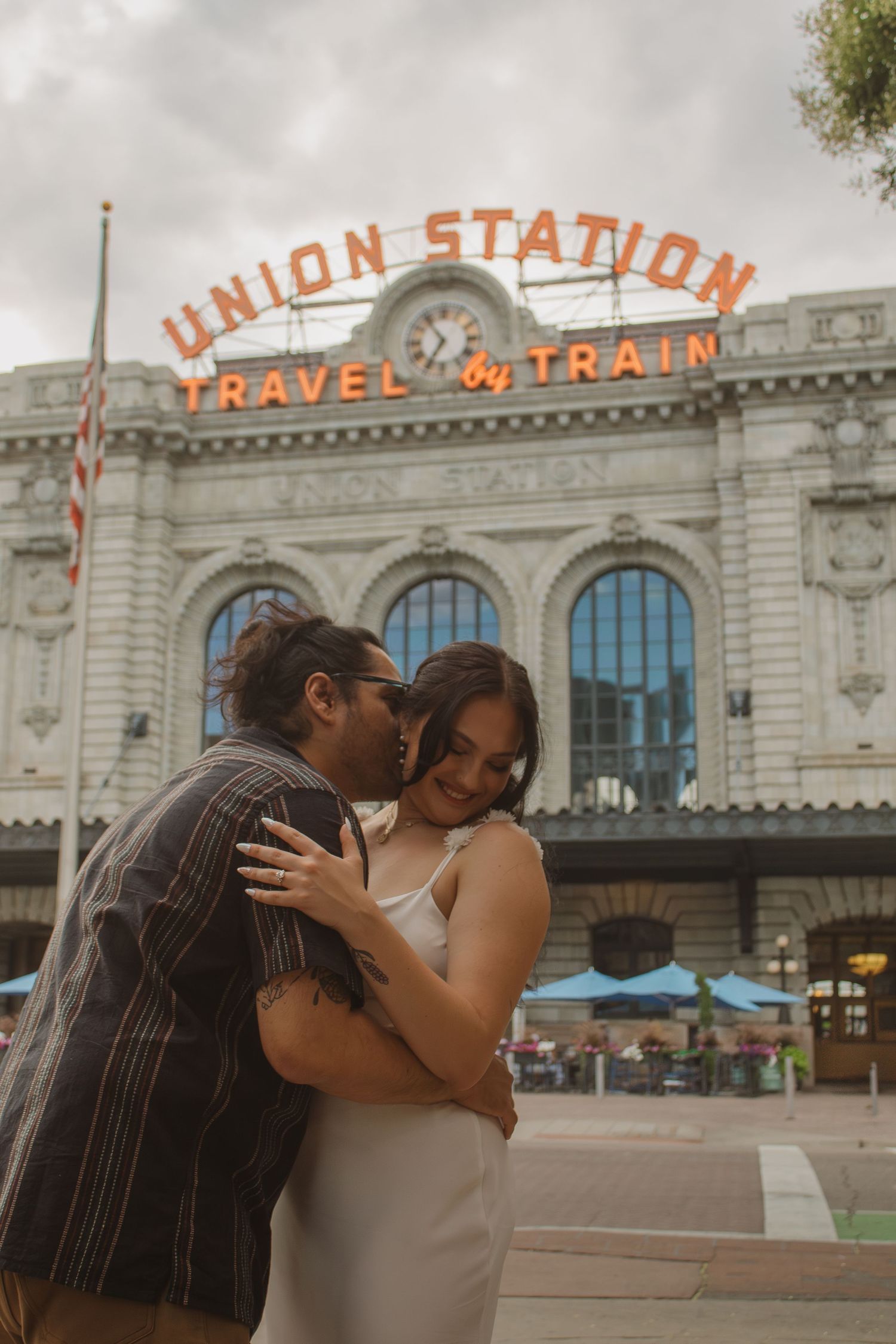 A couple embraces in front of Denver's historic Union Station building with iconic orange signage in the background.