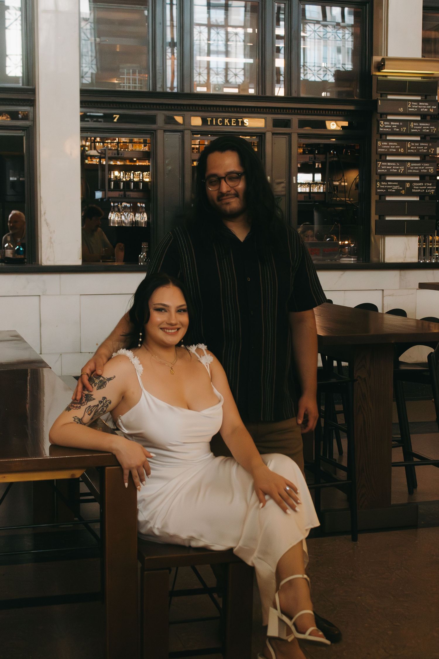Couple poses together in elegant interior with industrial-style windows and vintage decor.