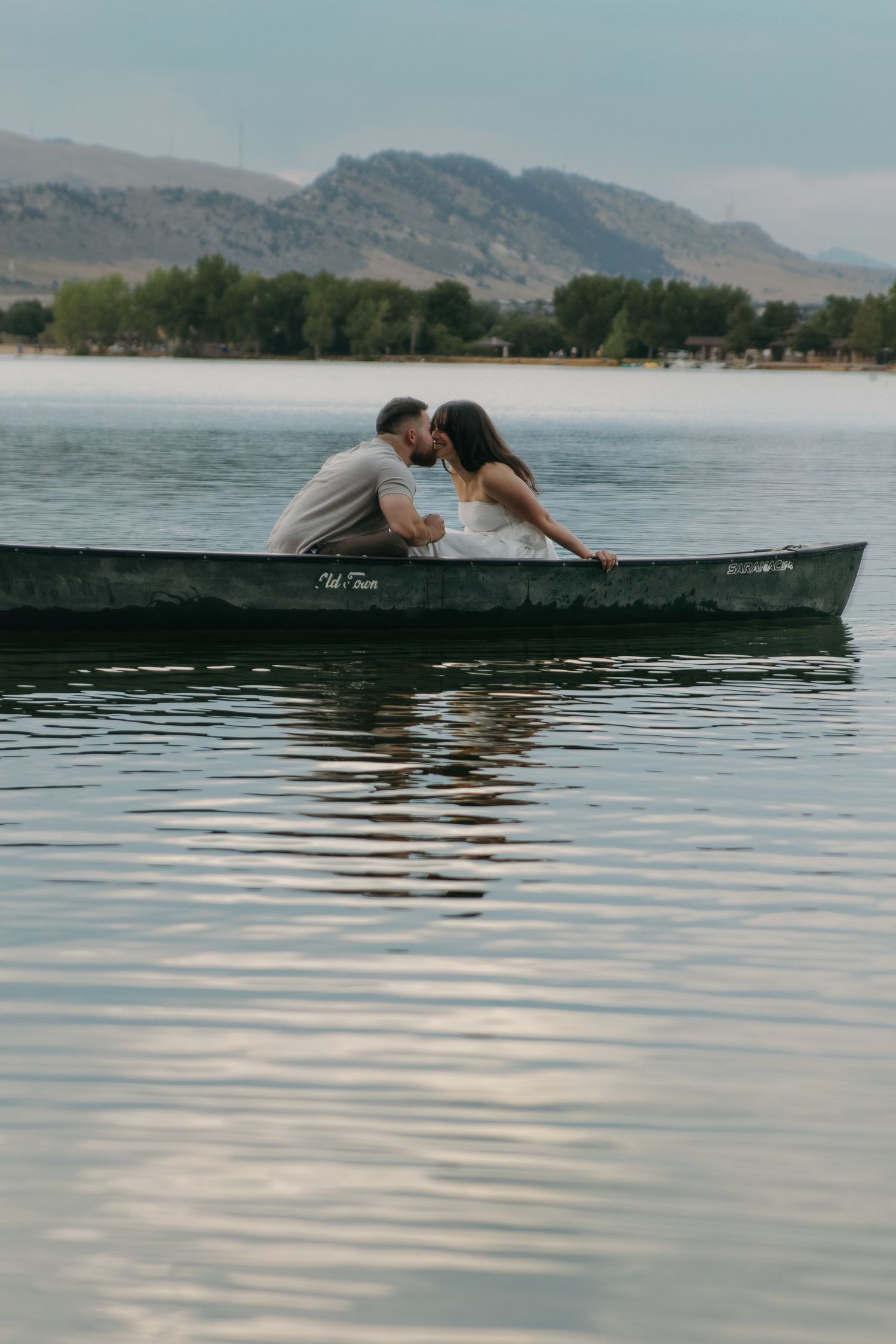 A couple shares a romantic moment in a canoe on a lake with mountains in the background.