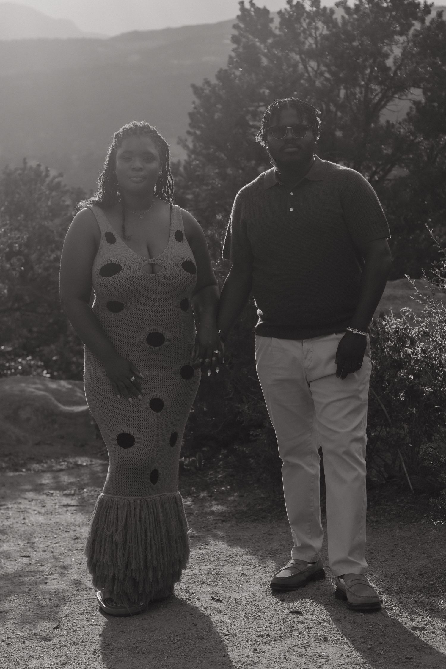 A couple poses together on a mountain trail in coordinated polka dot dress and brown sweater outfits.