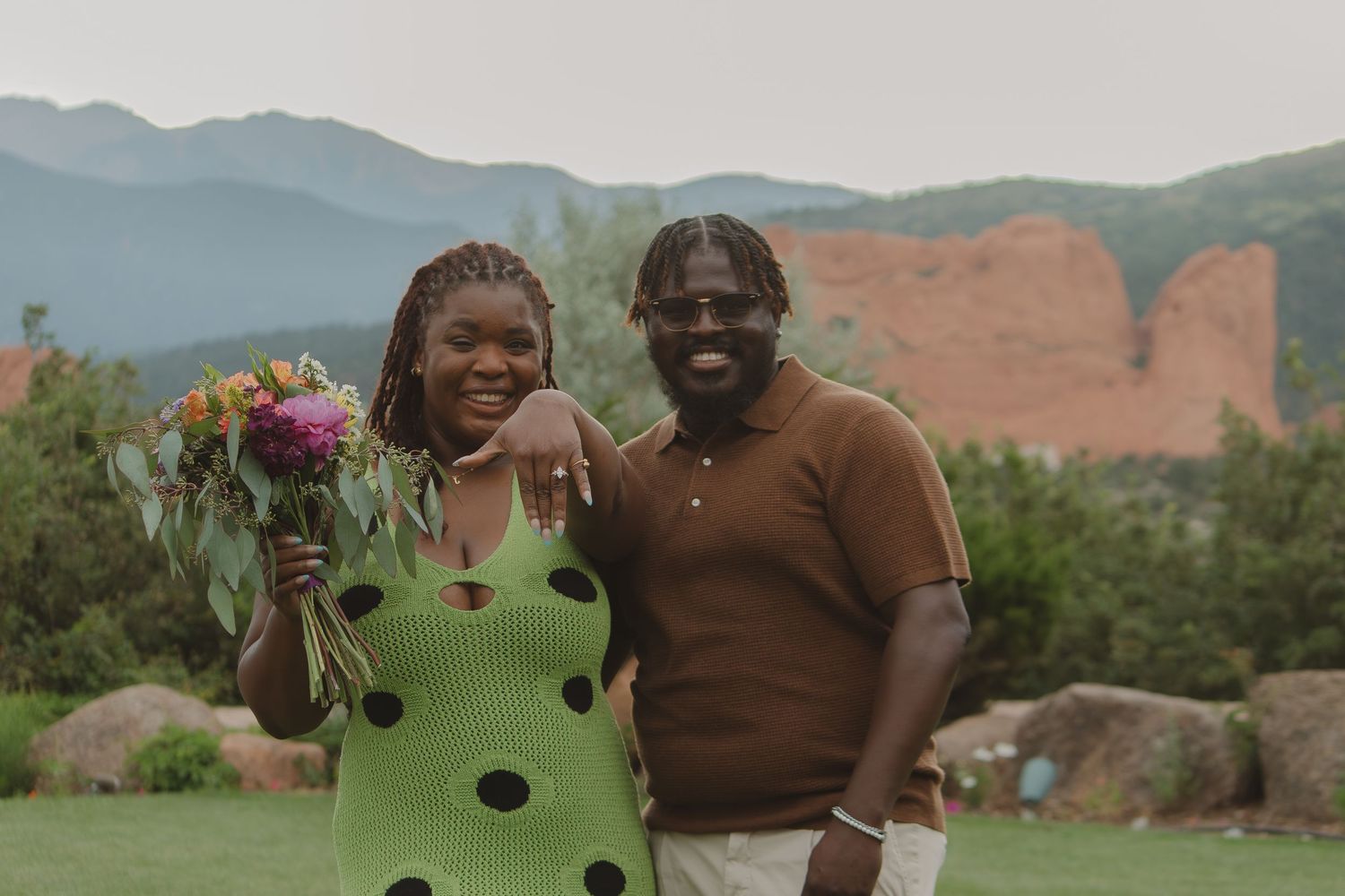A happy couple poses together outdoors with mountain views and red rocks in the background.