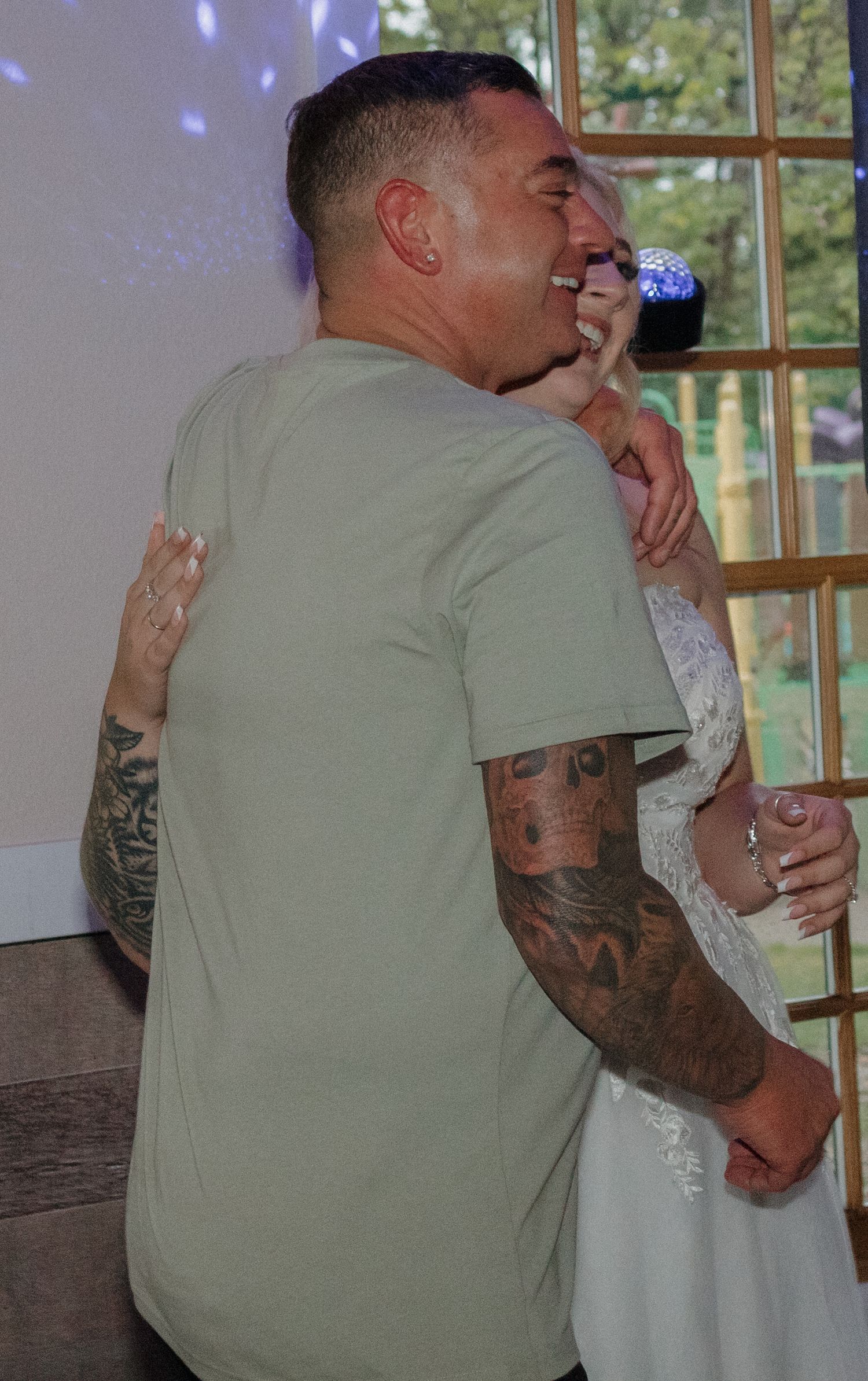 A couple embraces during a dance with blue lighting and windows in the background.
