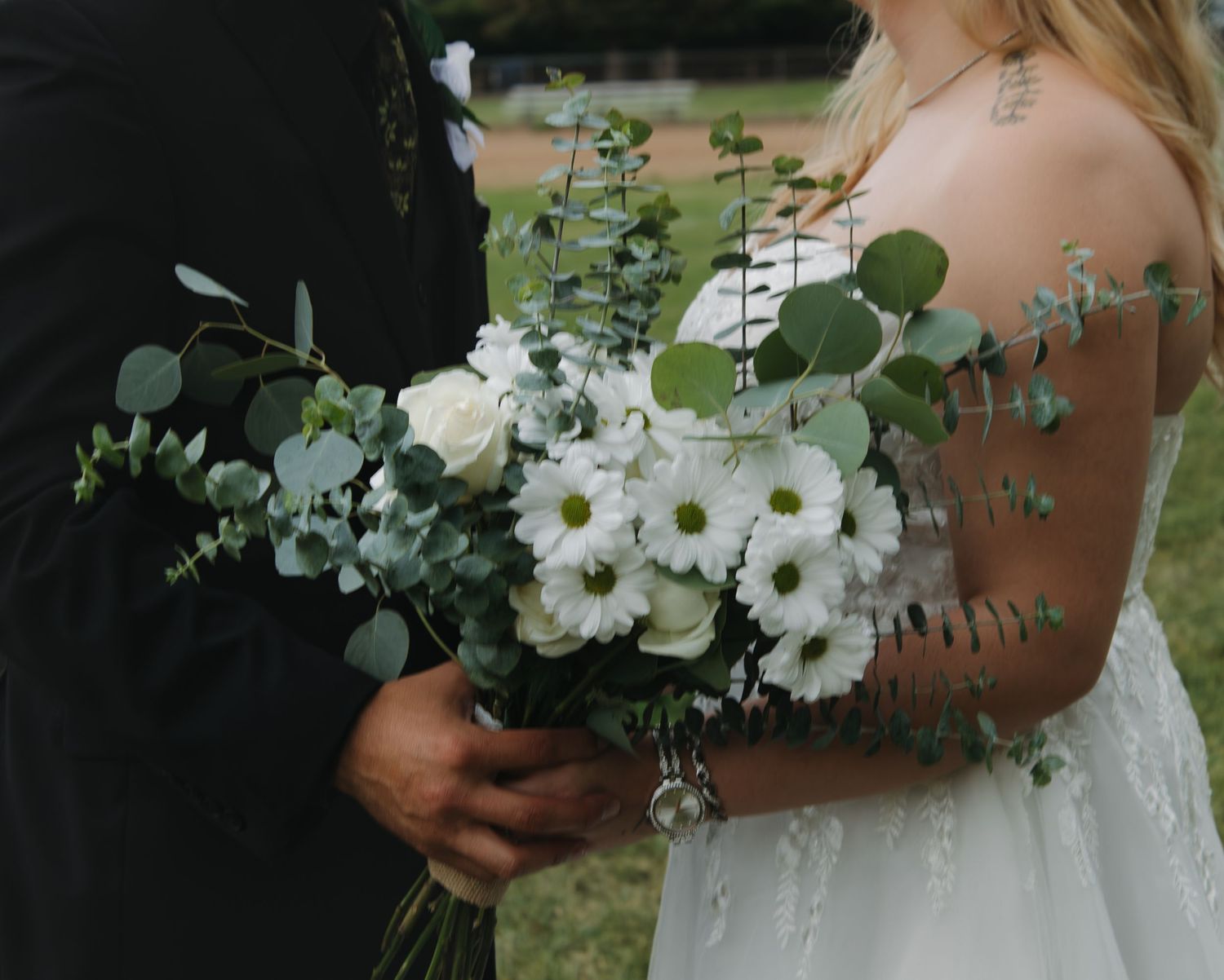 Close-up detail of a white floral bouquet with daisies and eucalyptus against a wedding dress.