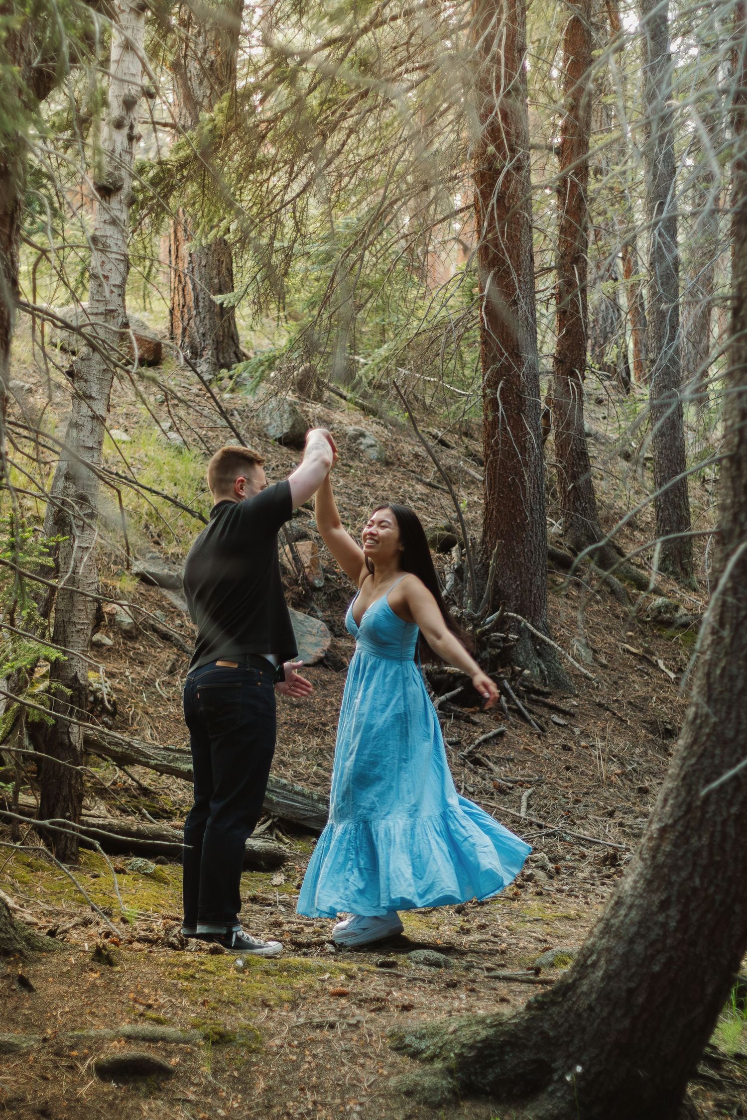 Two figures dance together on a forest trail surrounded by tall pine trees.