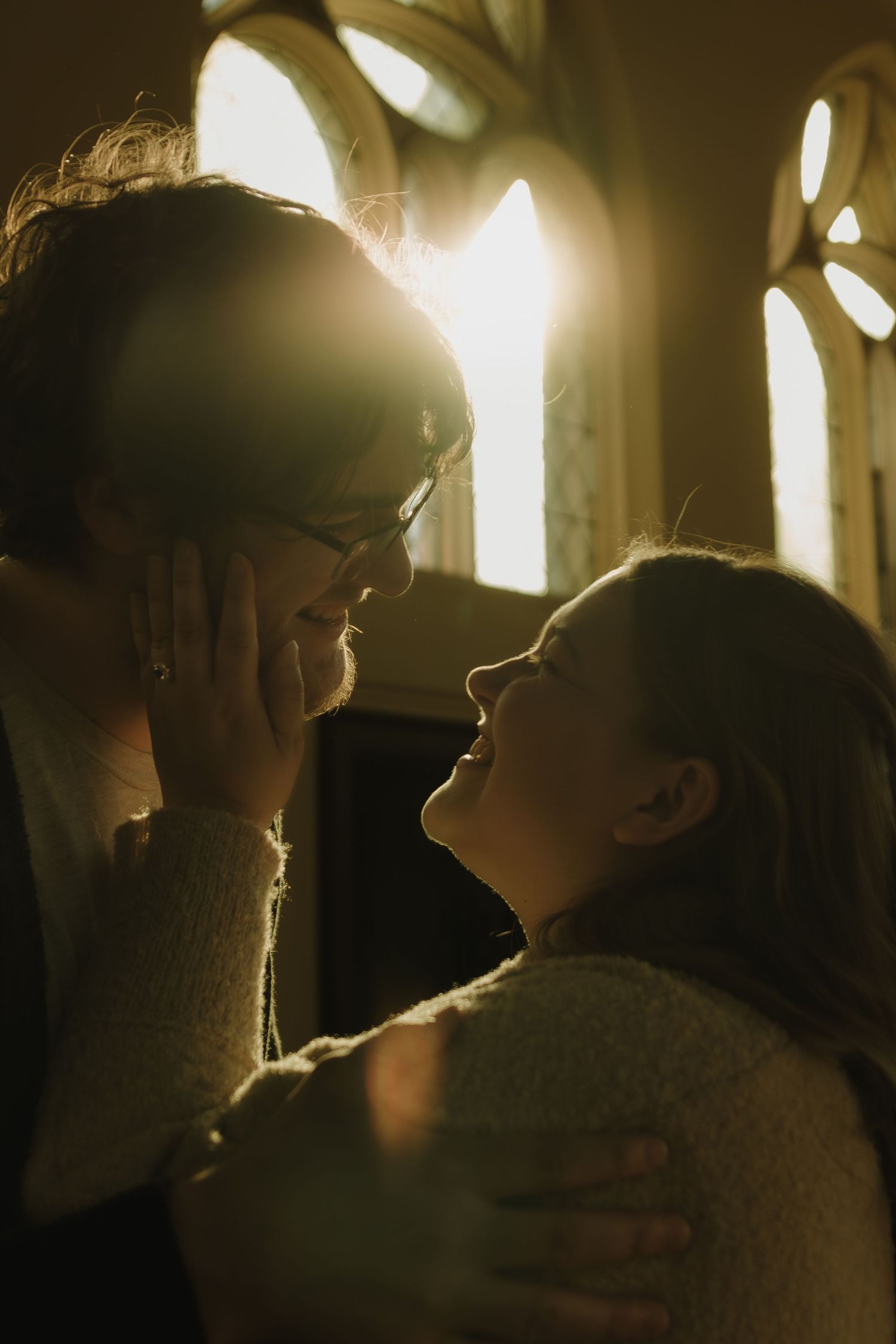 Two silhouetted figures in intimate conversation backlit by warm glowing window light.