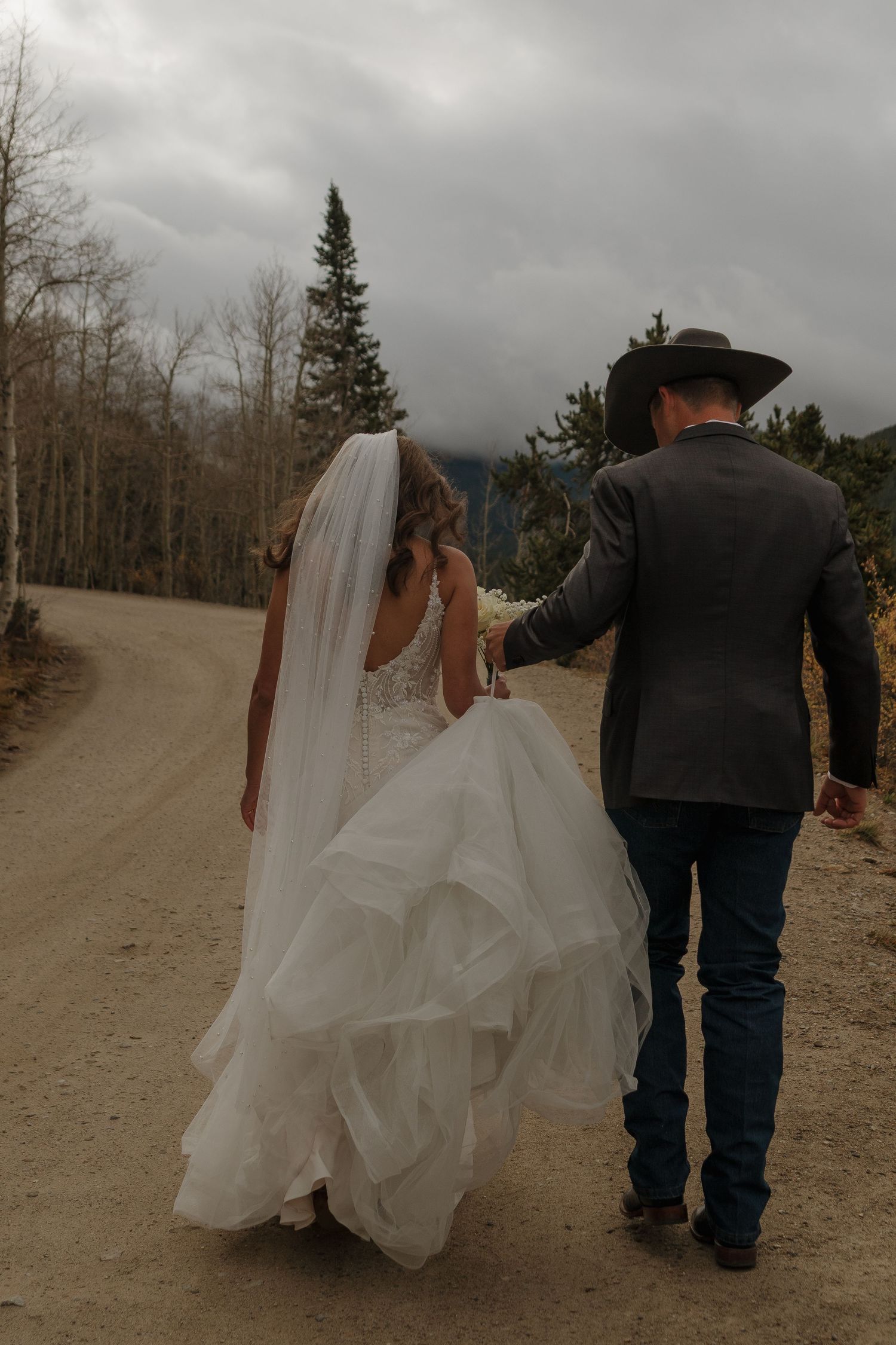 A couple walks hand in hand down a mountain path, with the bride's dress flowing behind them.