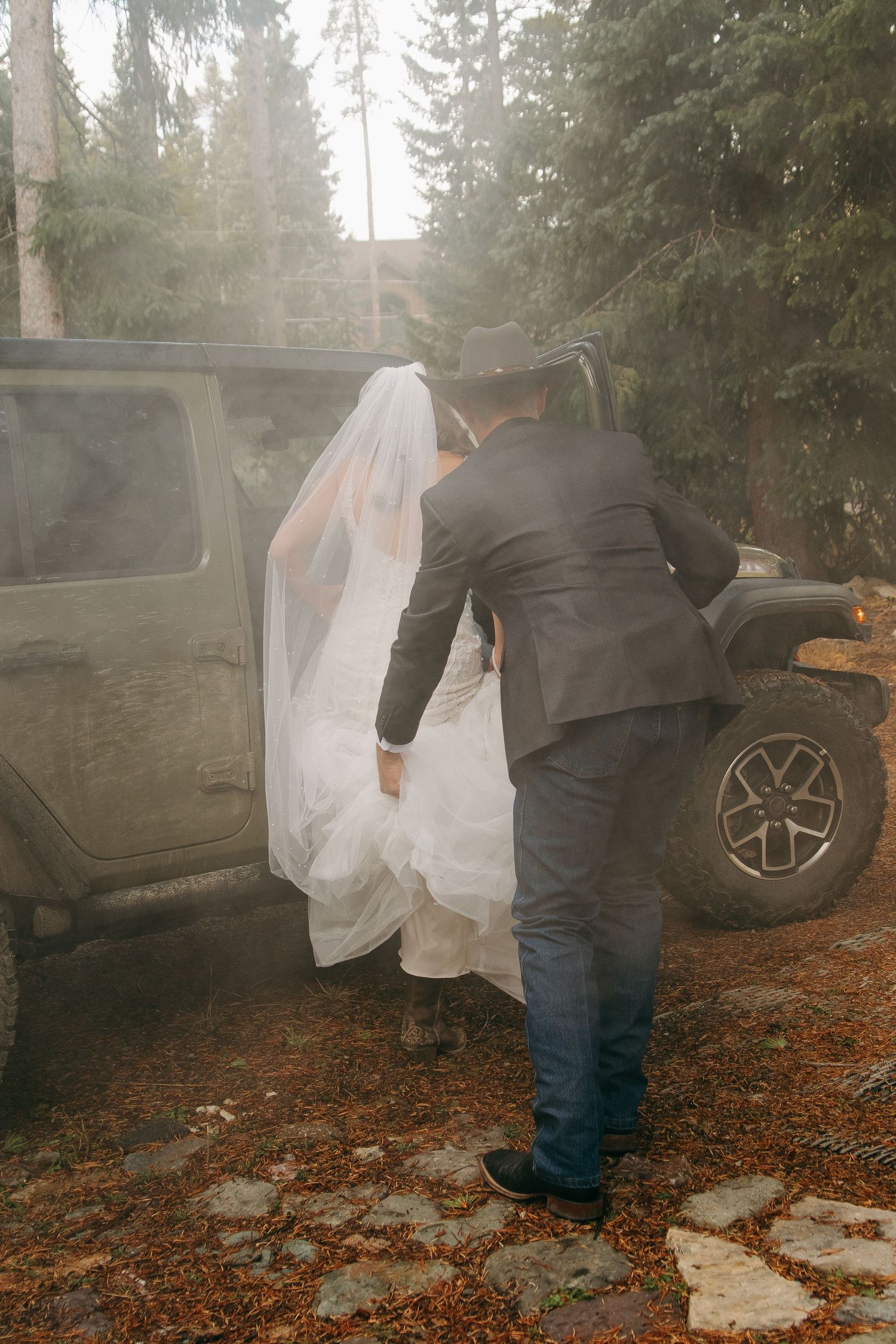 A misty forest wedding scene with a couple getting into their getaway car.
