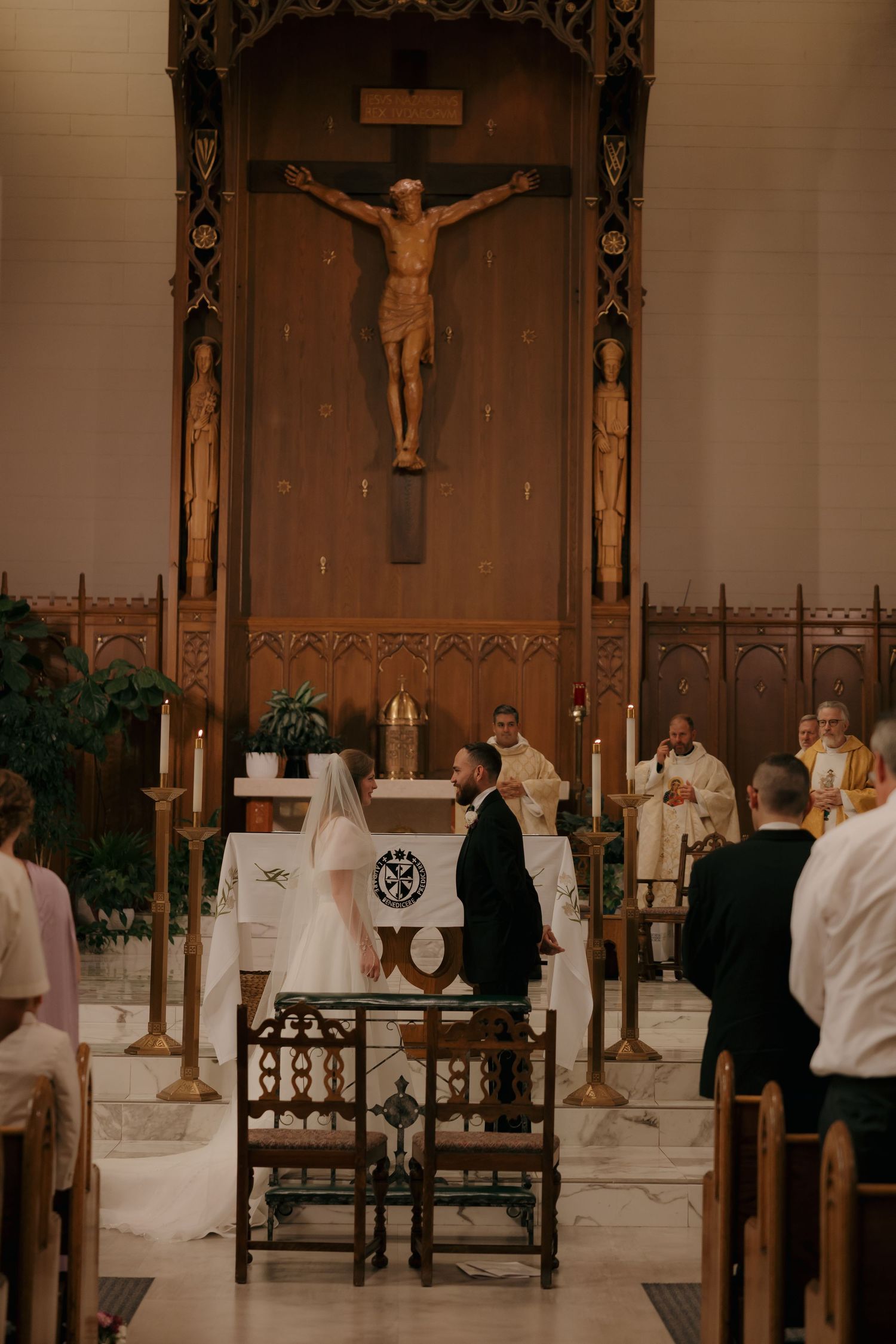 Bride and groom stand at altar beneath crucifix during Catholic wedding ceremony.