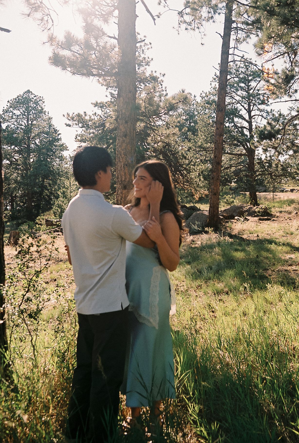 Couple sharing a romantic moment in a sunlit forest clearing, woman in mint dress, man in white shirt.