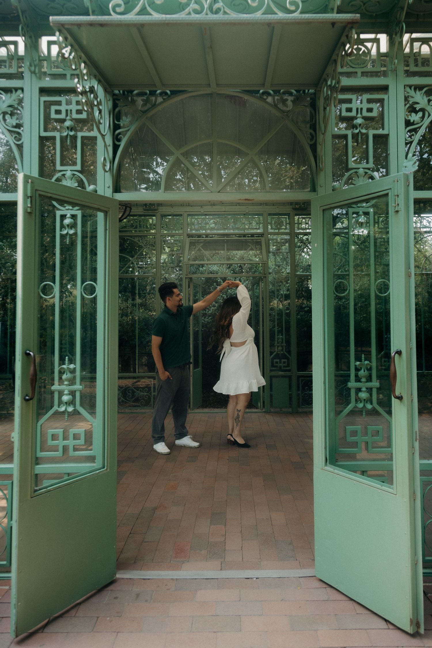 Couple dancing together in the doorway of an ornate green iron greenhouse entrance.