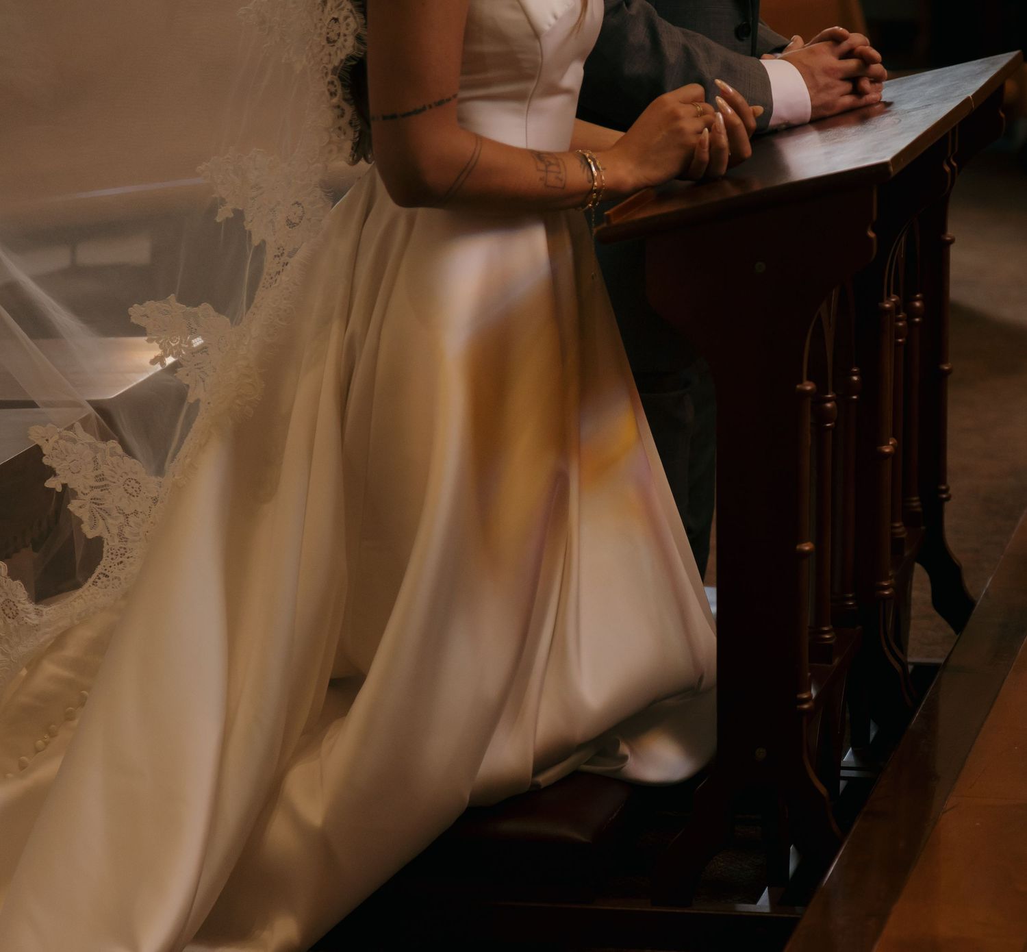 Close-up of bride in elegant white gown kneeling at wooden altar during church wedding ceremony.