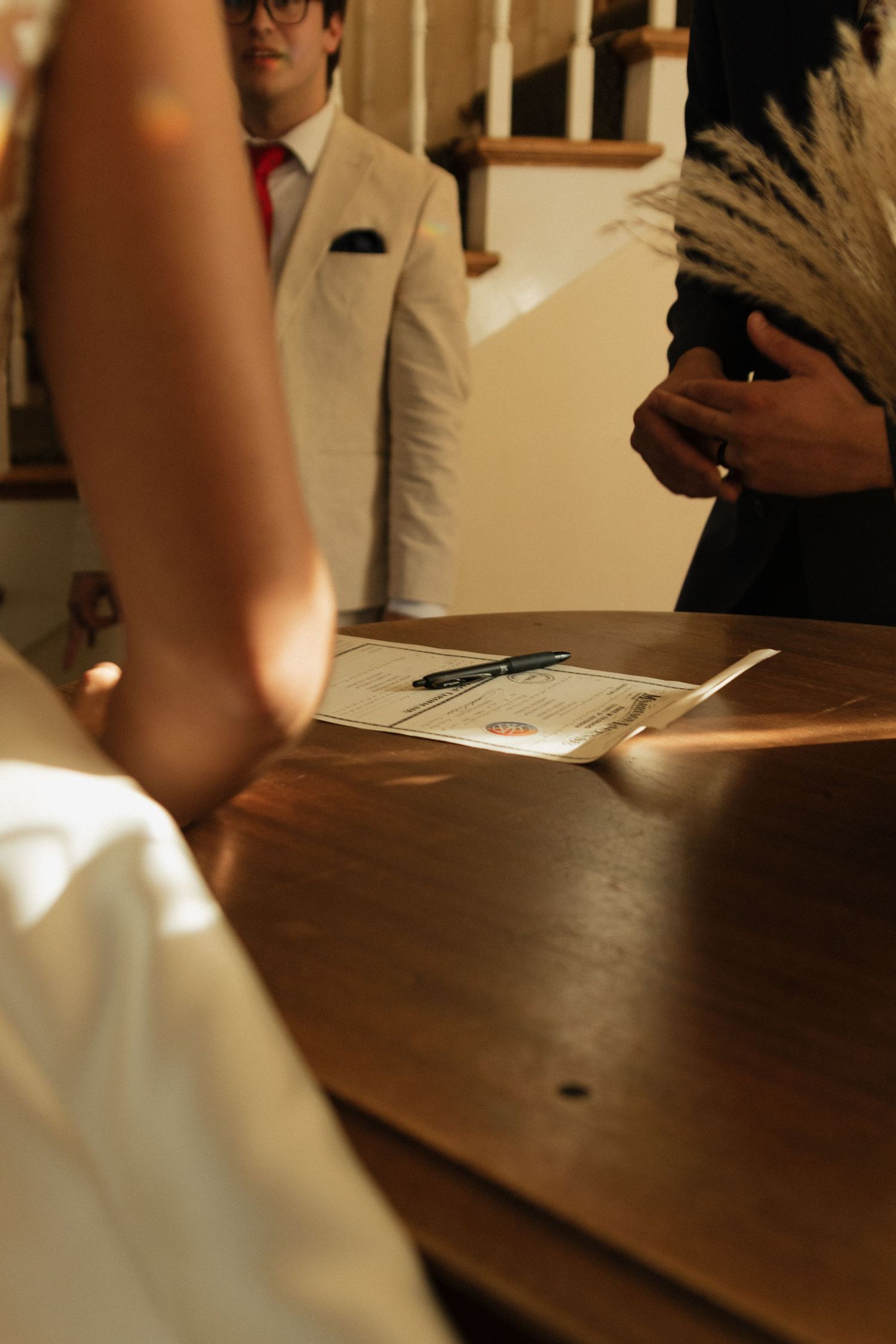 Candid wedding moment captured at wooden table during document signing.