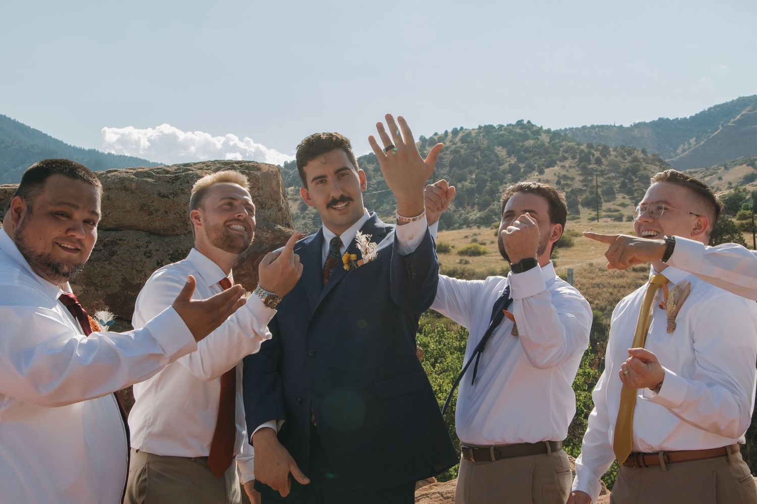 Wedding party members wave and pose joyfully against a scenic mountain backdrop.