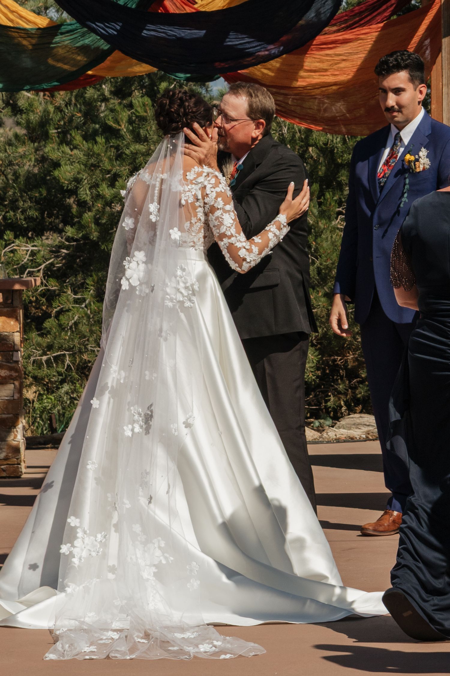 Flowing white wedding dress train with delicate lace details trailing behind on outdoor stone patio.