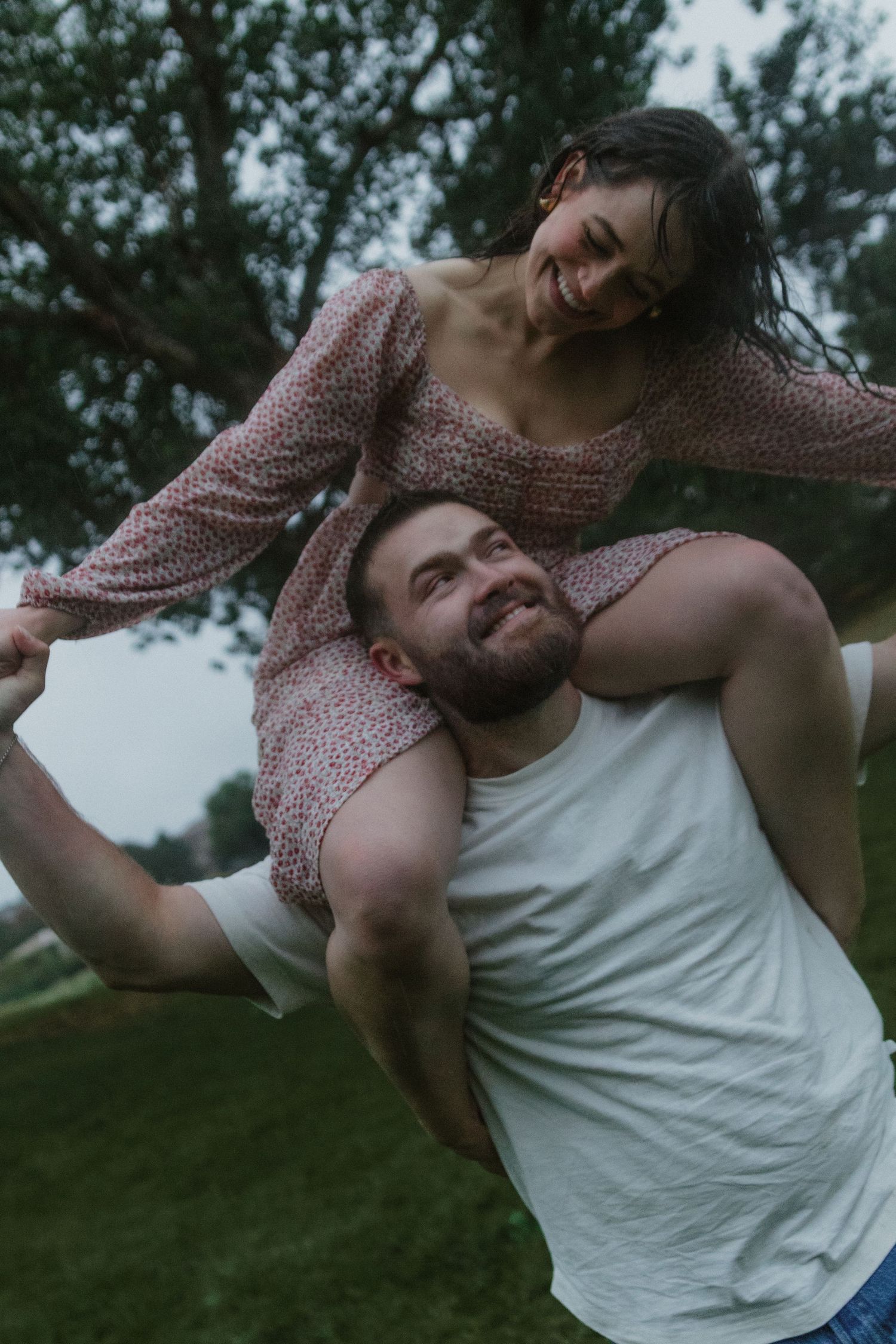A couple shares a playful piggyback ride moment outdoors against a nature backdrop.
