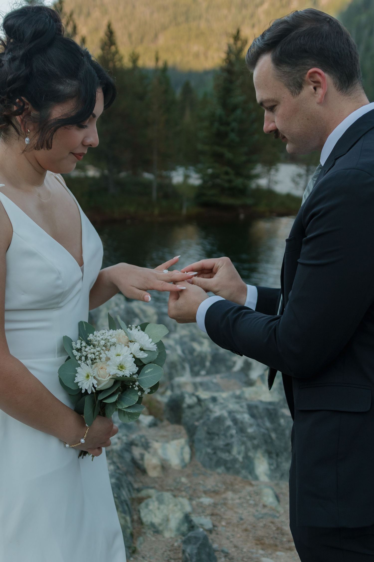 A couple exchanges rings during an intimate lakeside wedding ceremony with mountains in the background.