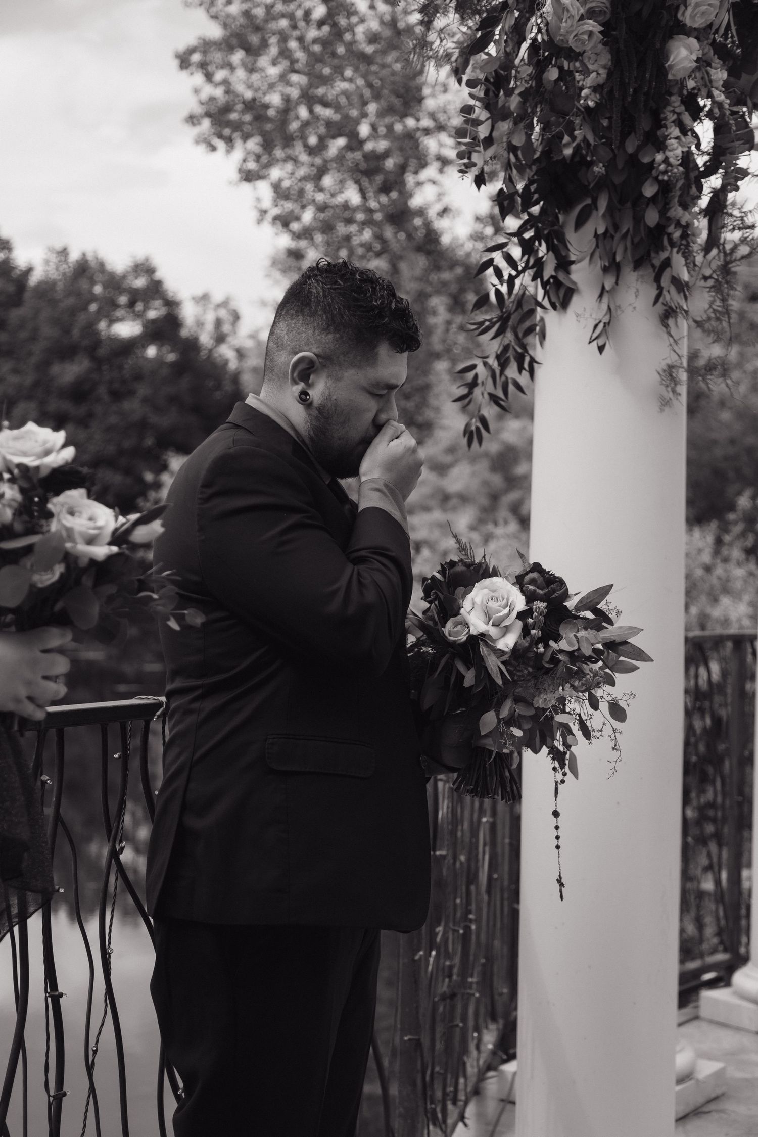 Emotional groom crying at wedding altar surrounded by floral arrangements in black and white photo.