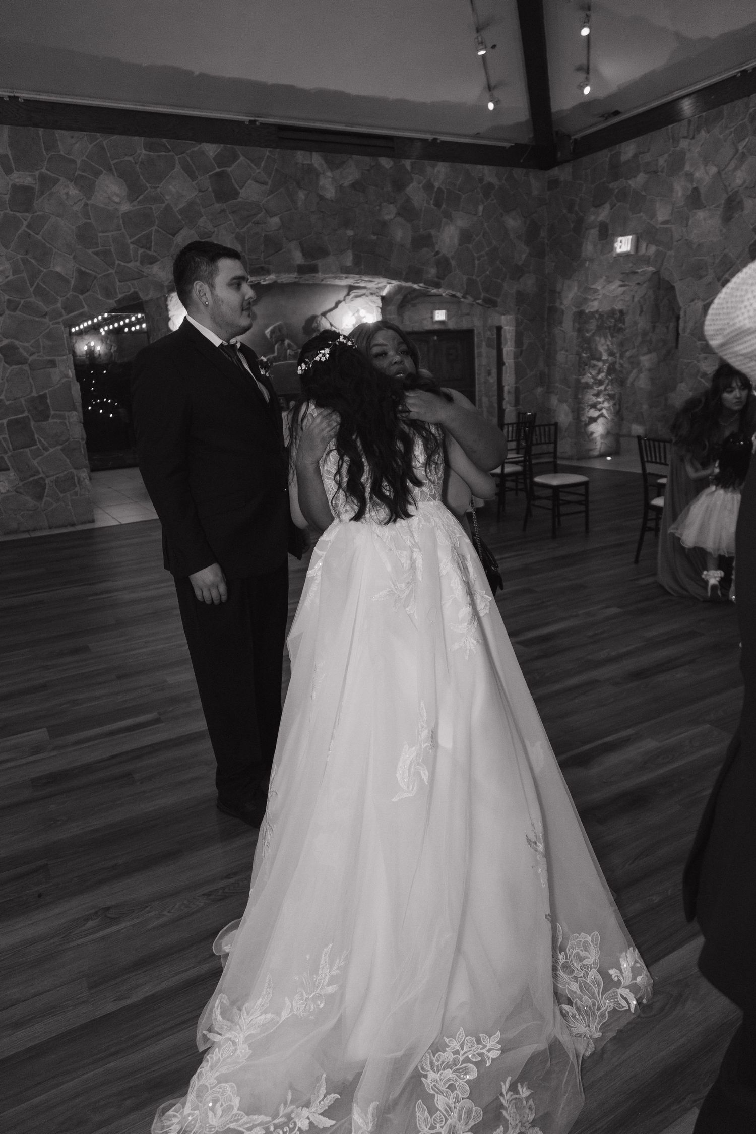 Black and white photo of a bride and groom sharing their first dance in a rustic stone-walled ballroom.