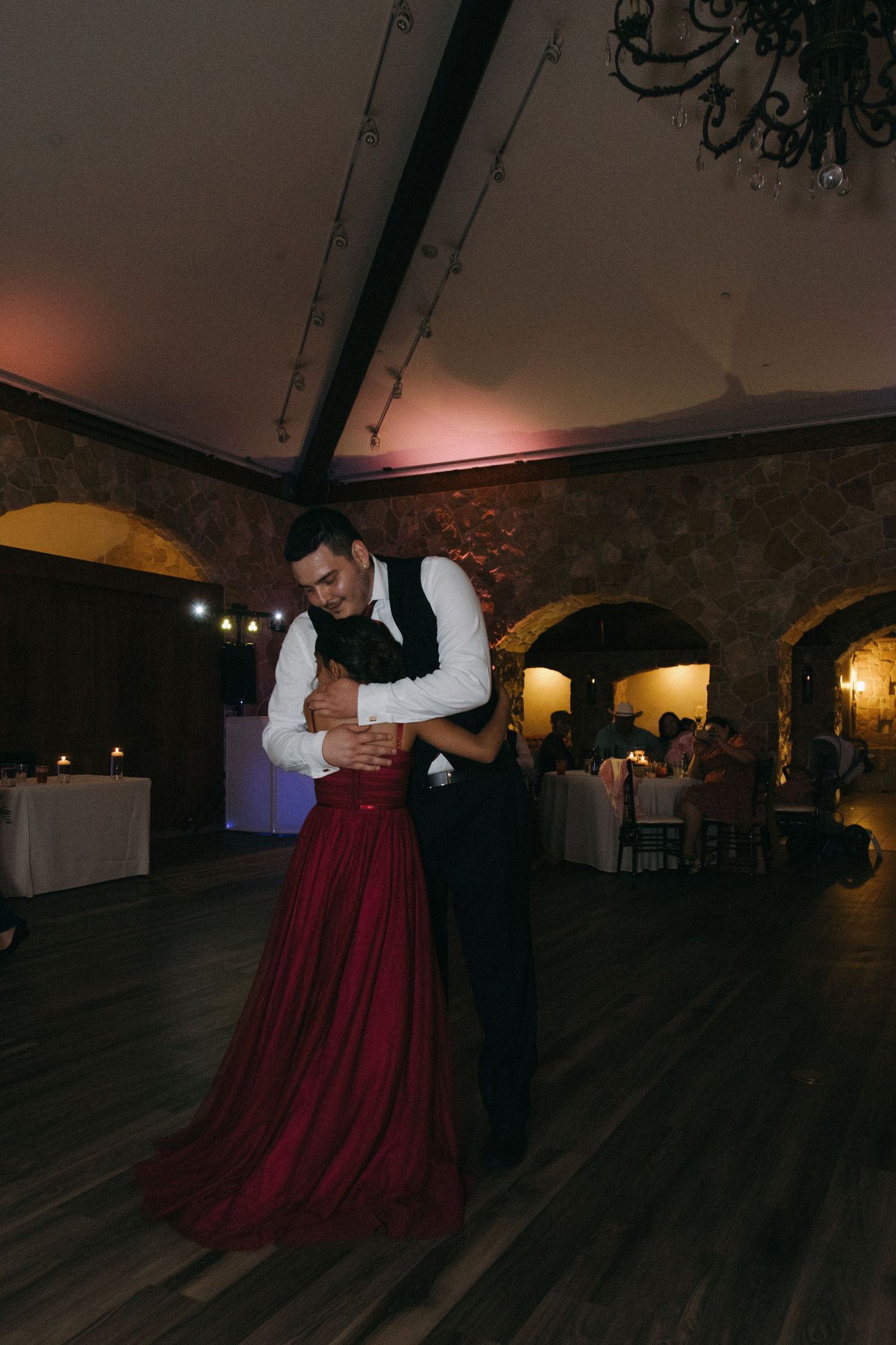 Groom in white shirt and vest sharing a romantic slow dance with partner in red gown.