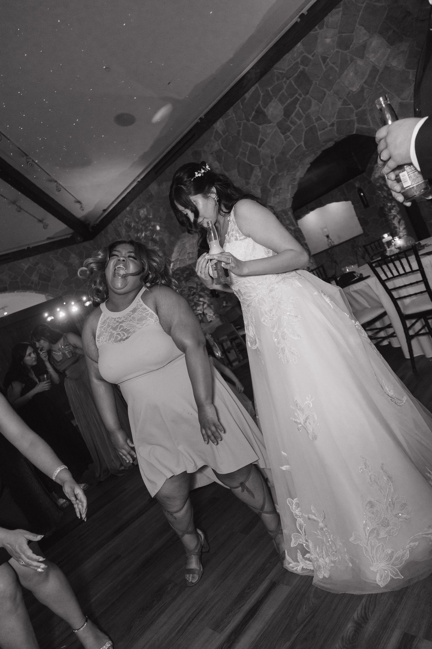 Bride and guest dance joyfully together on the wedding reception dance floor in black and white photo.