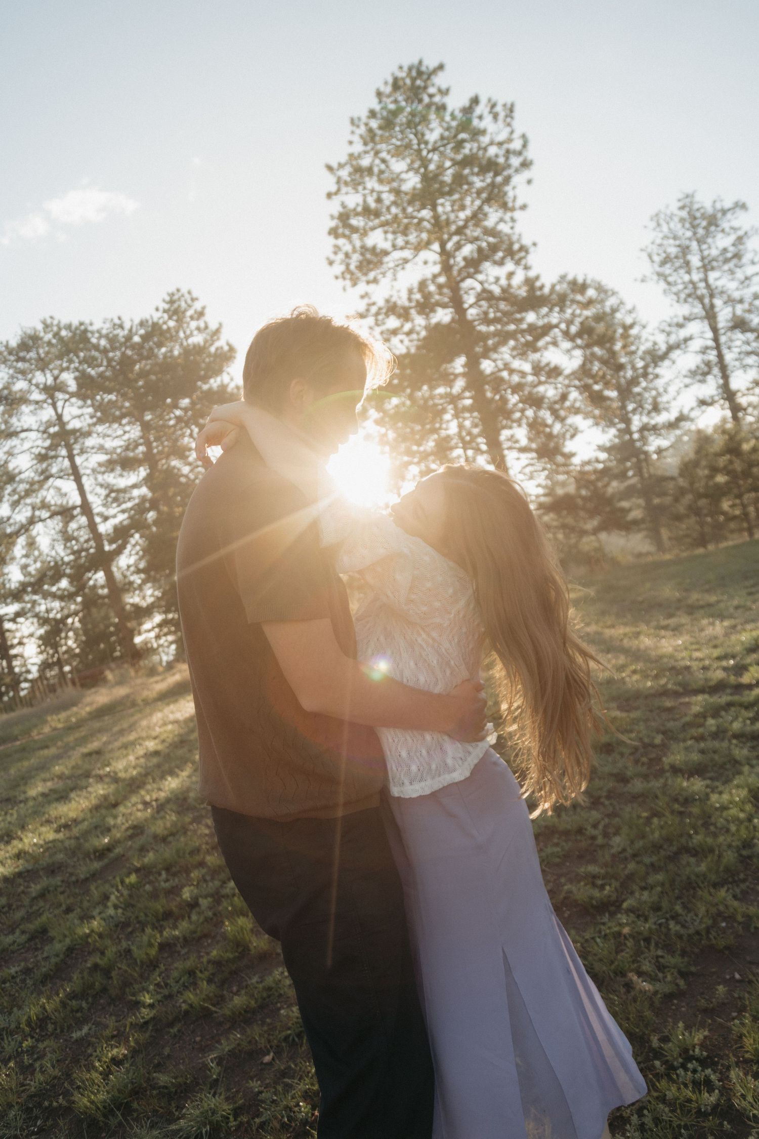 Couple embracing with stunning golden sun flare between them in a pine tree landscape.