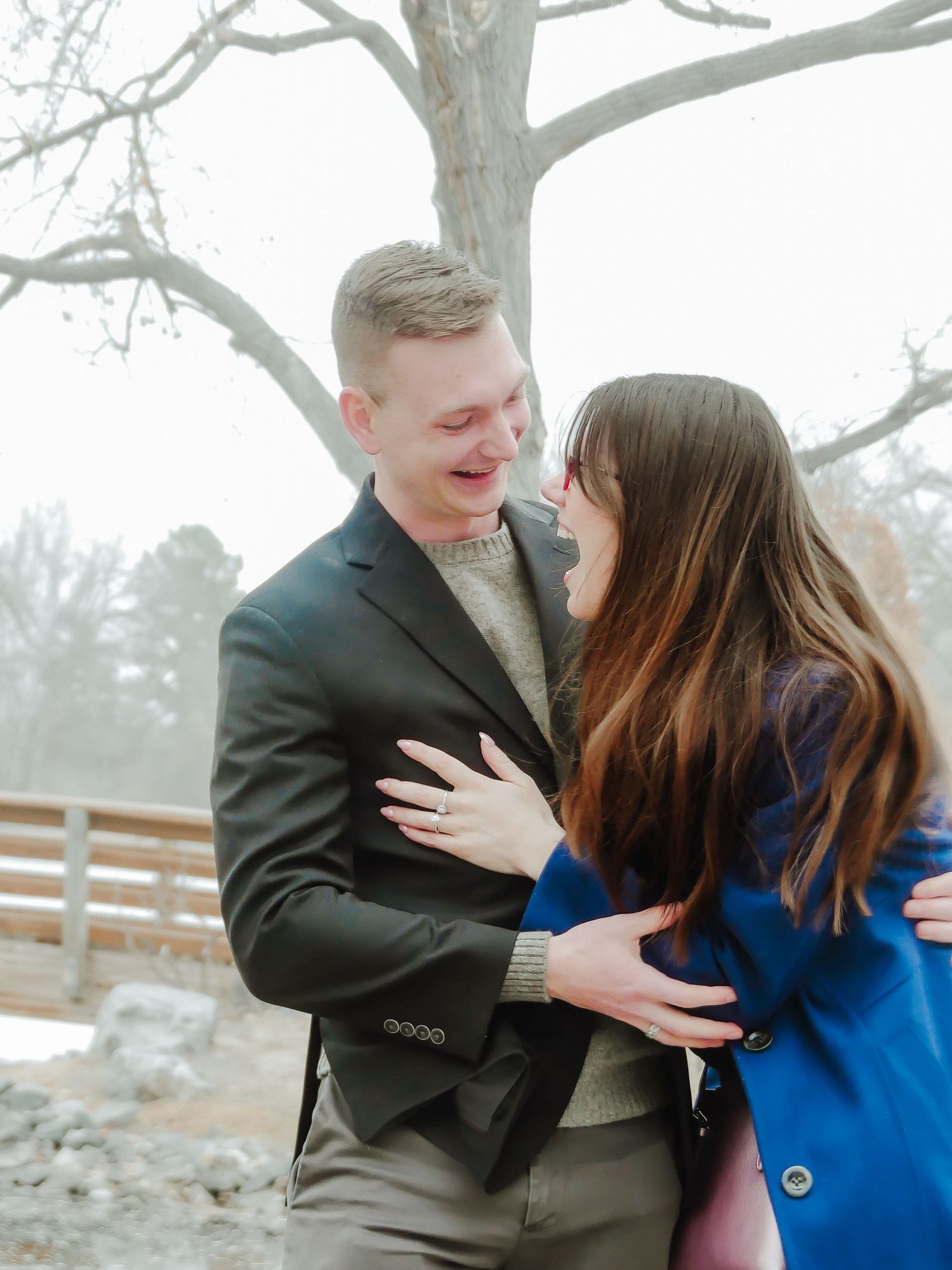 A couple shares a tender embrace outdoors on a misty winter day.