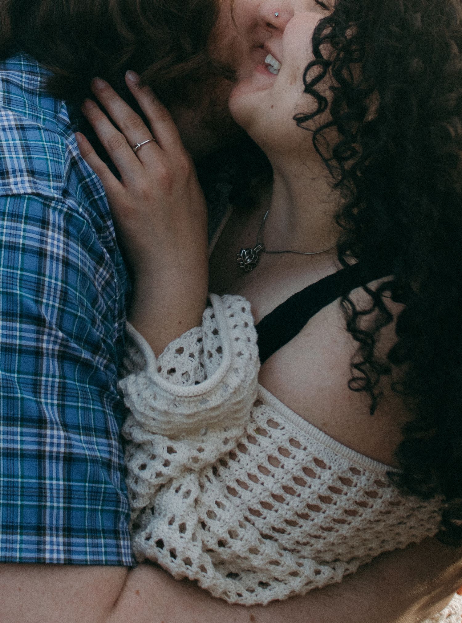 Close-up shot of a couple embracing, showing details of a crocheted white top and plaid shirt.