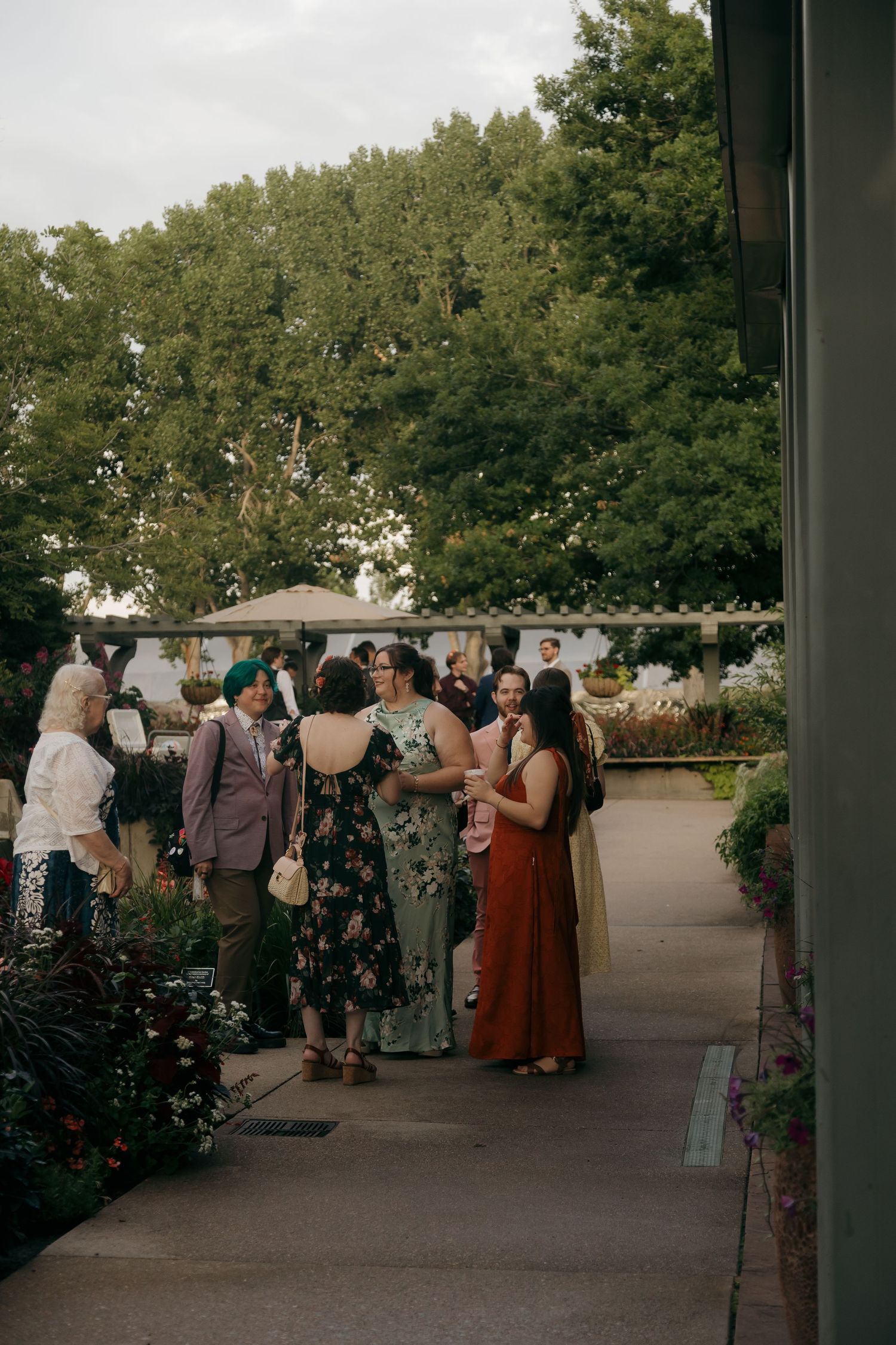 Wedding guests mingle outdoors on garden pathway in colorful formal attire at reception.