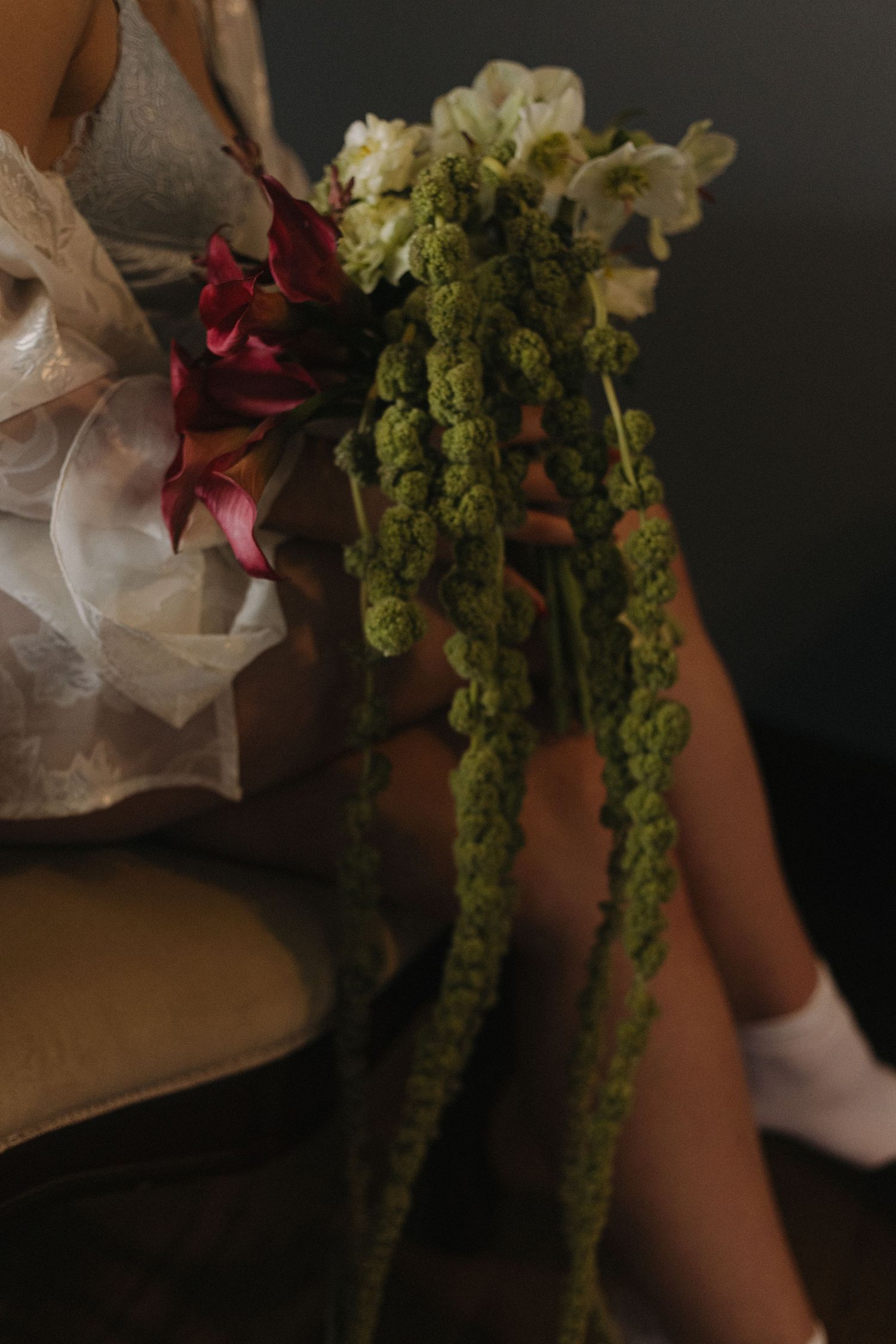 Wedding bouquet with deep red flowers and trailing green foliage against dark background.