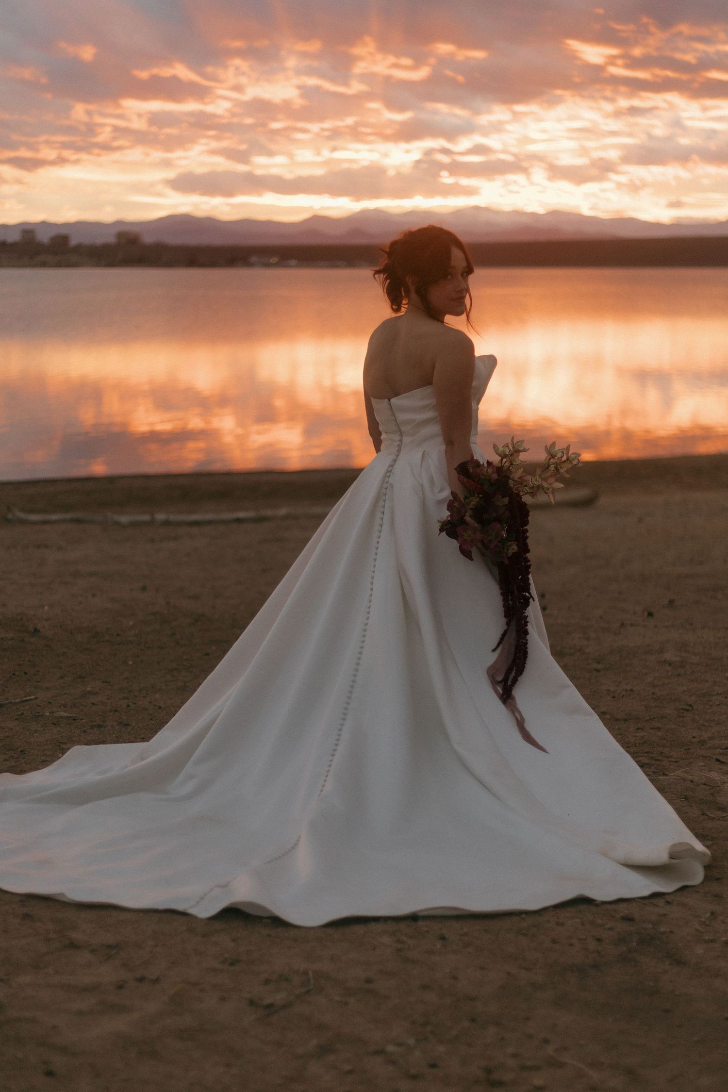 A flowing white wedding dress trails across desert terrain during golden hour sunset.