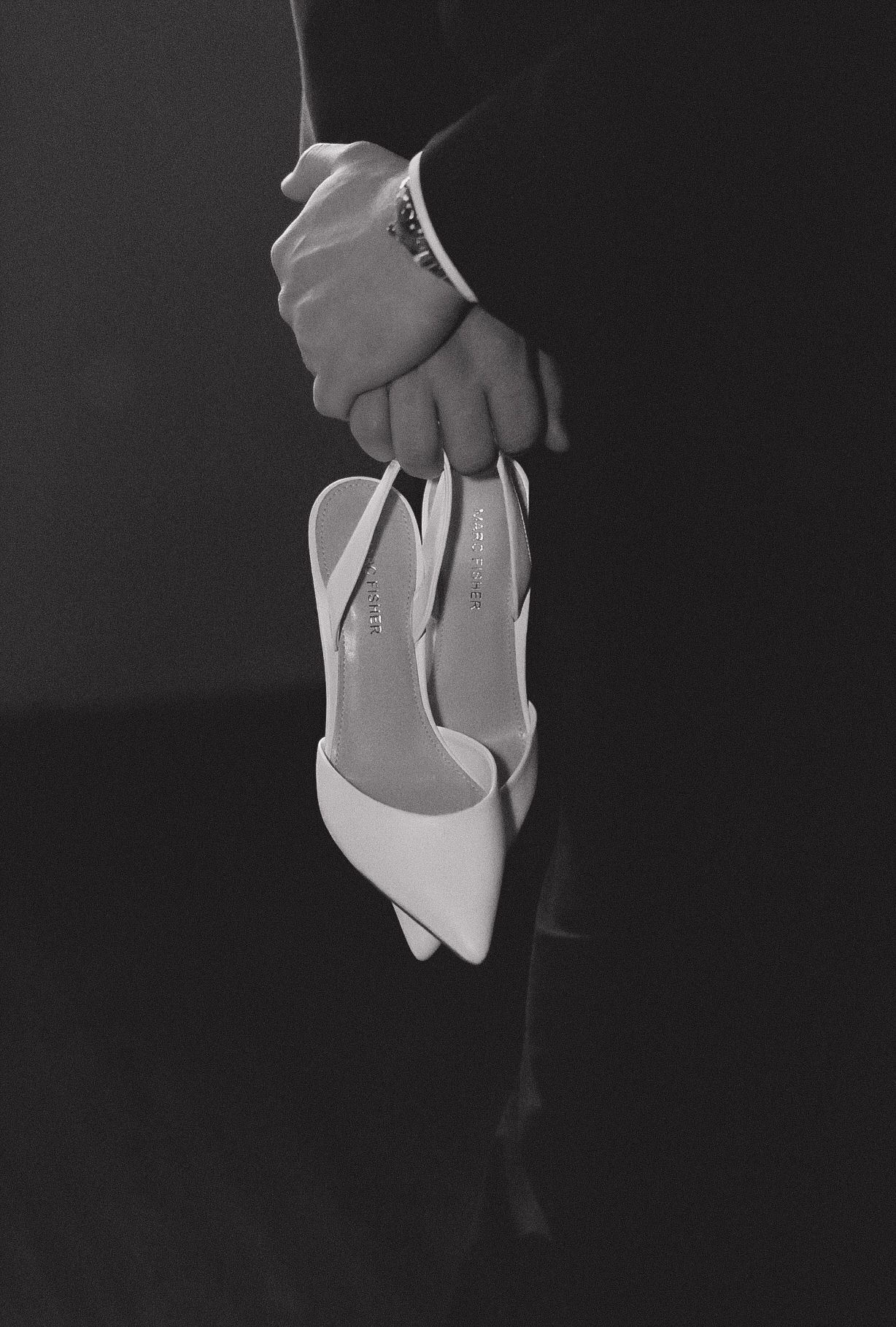Black and white detail shot of hands holding white bridal shoes.