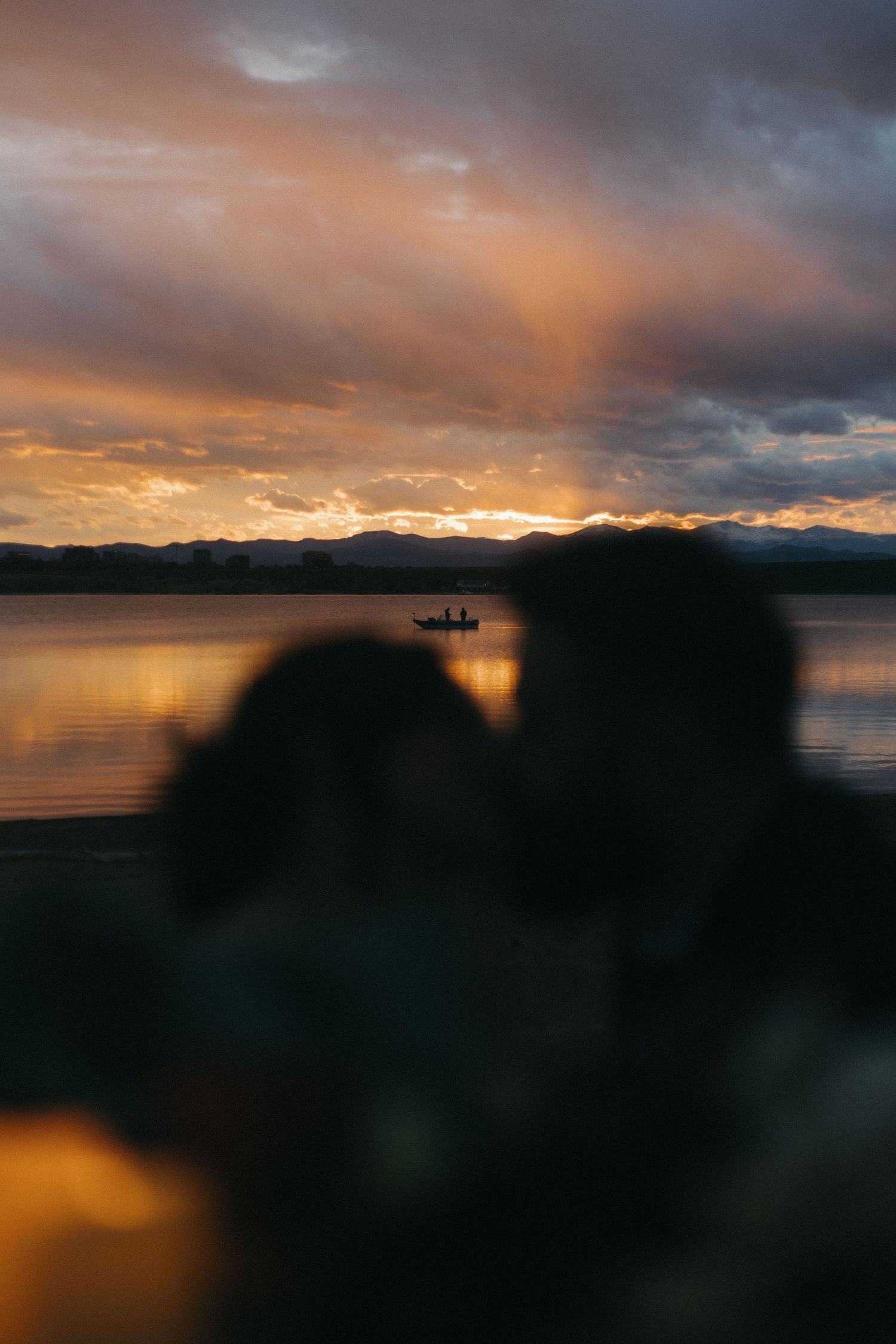 Silhouettes against a dramatic sunset over a lake with mountains in the background.