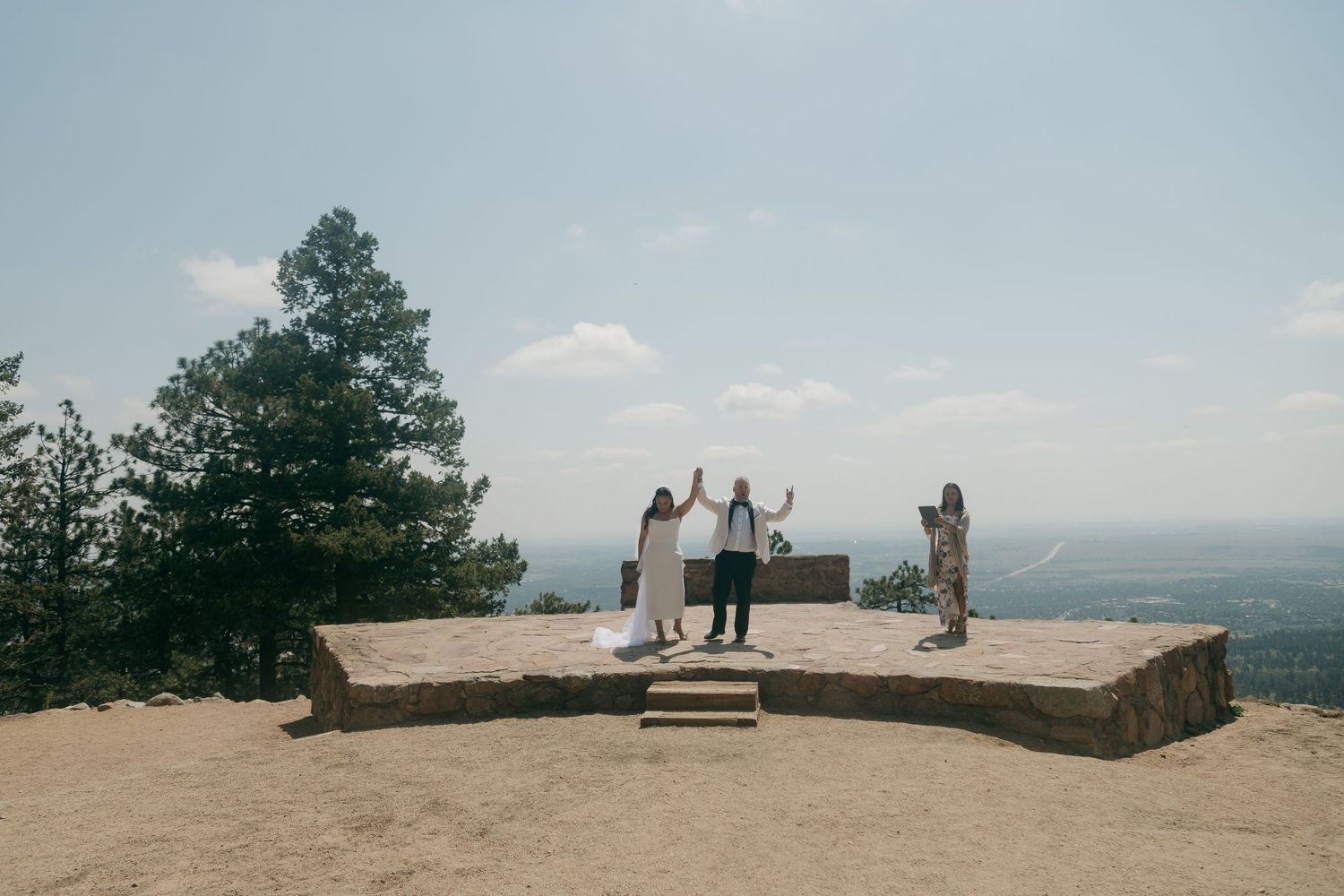 Wedding ceremony on a rocky mountaintop overlook with sweeping valley views under hazy sky.