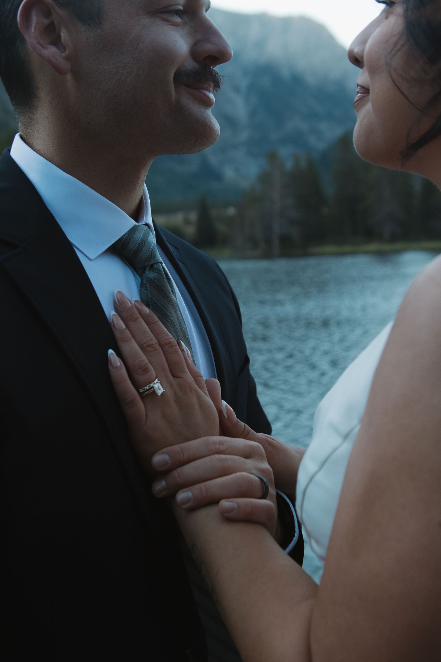 Romantic close-up of couple embracing by a lake with mountains in background during sunset.
