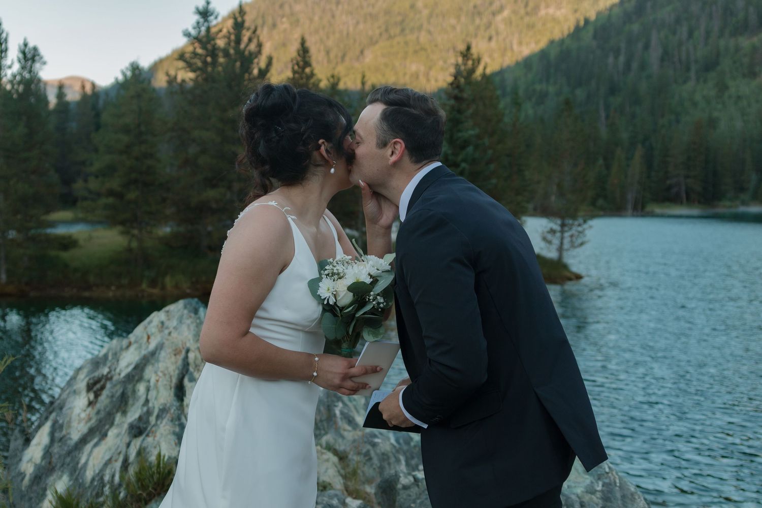 An intimate outdoor wedding moment captured against a backdrop of mountains and a tranquil lake.