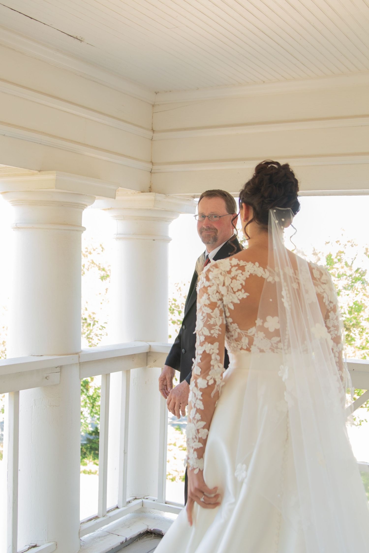 Wedding couple shares intimate moment on white porch during first look.