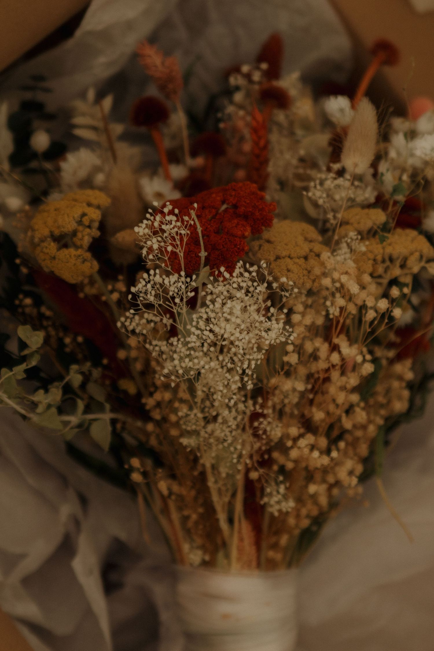 A dried flower bouquet featuring red and white blooms with baby's breath wrapped in delicate paper.
