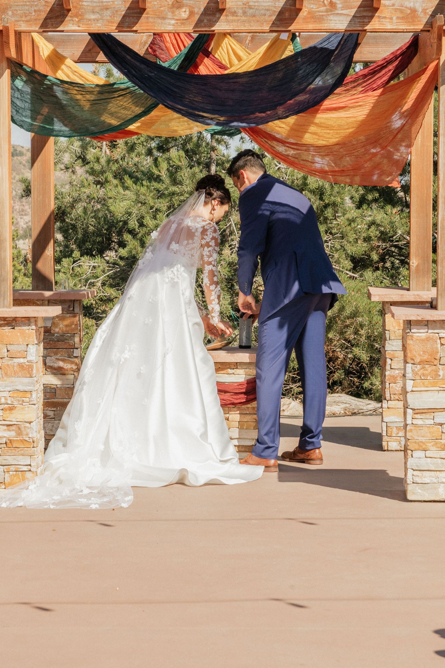 Wedding ceremony view under draped fabric pergola with stone columns and mountain backdrop.