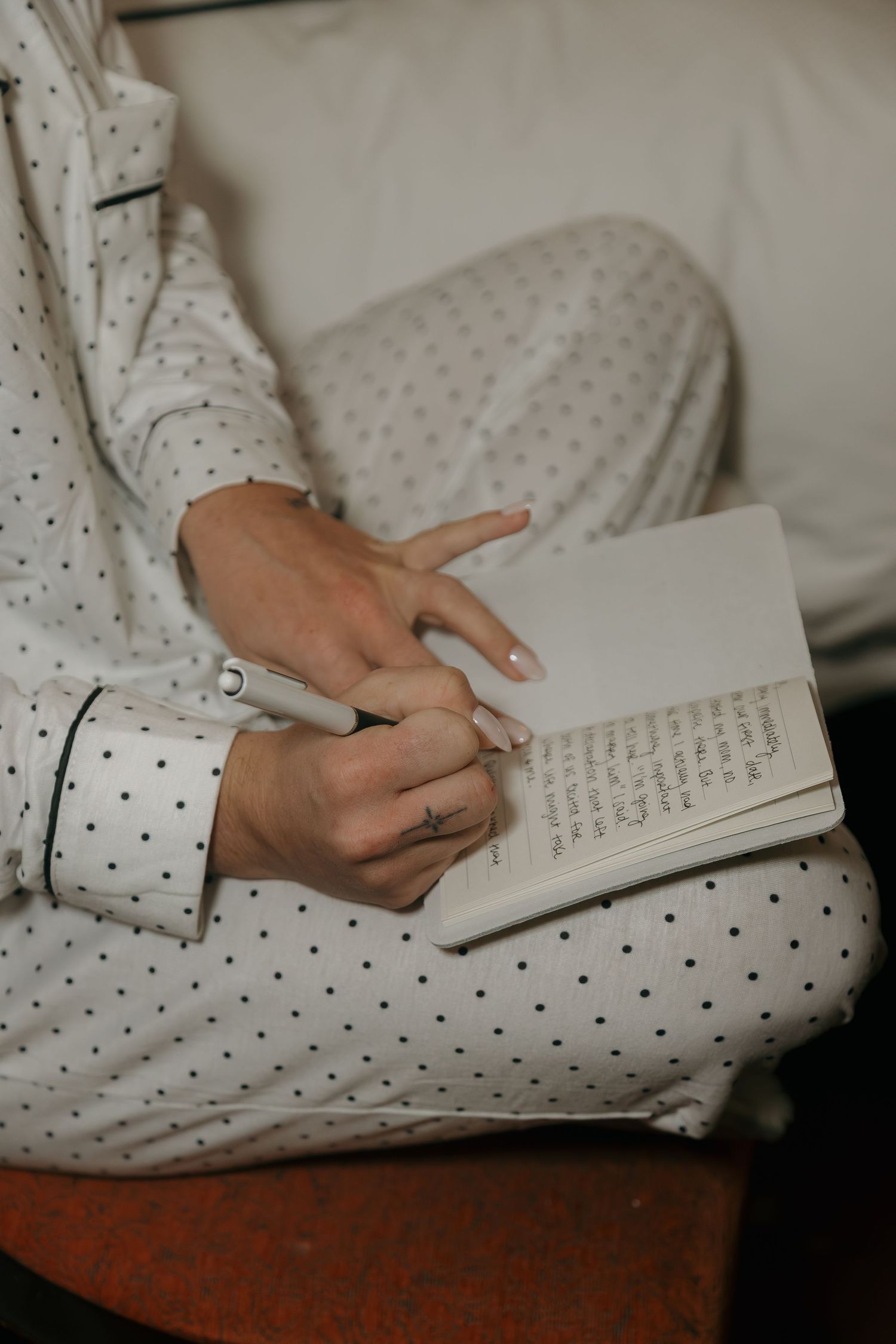 A woman in polka dot pajamas writing in a journal while seated on a couch.