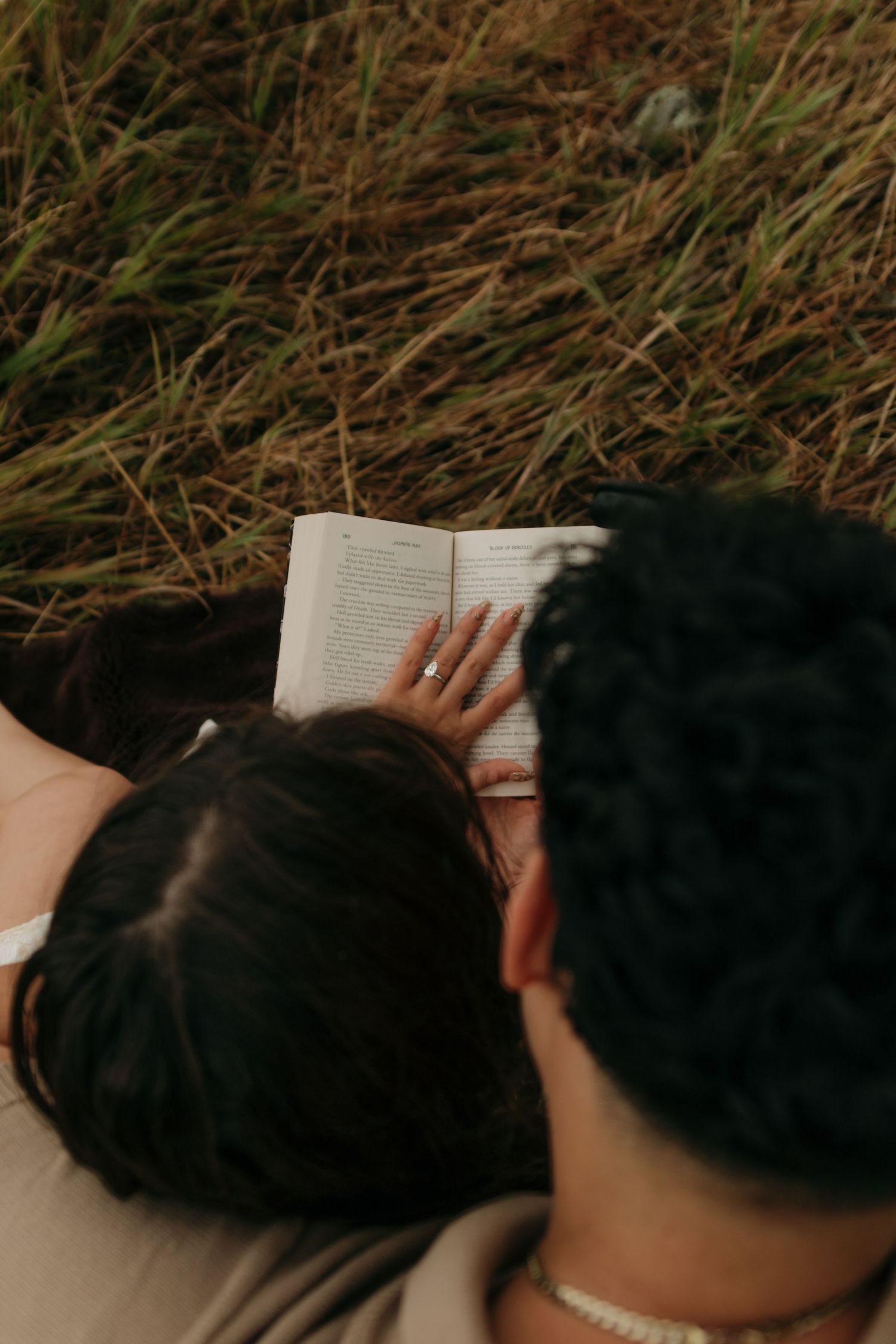 Overhead view of couple lying in grass together reading a book outdoors.