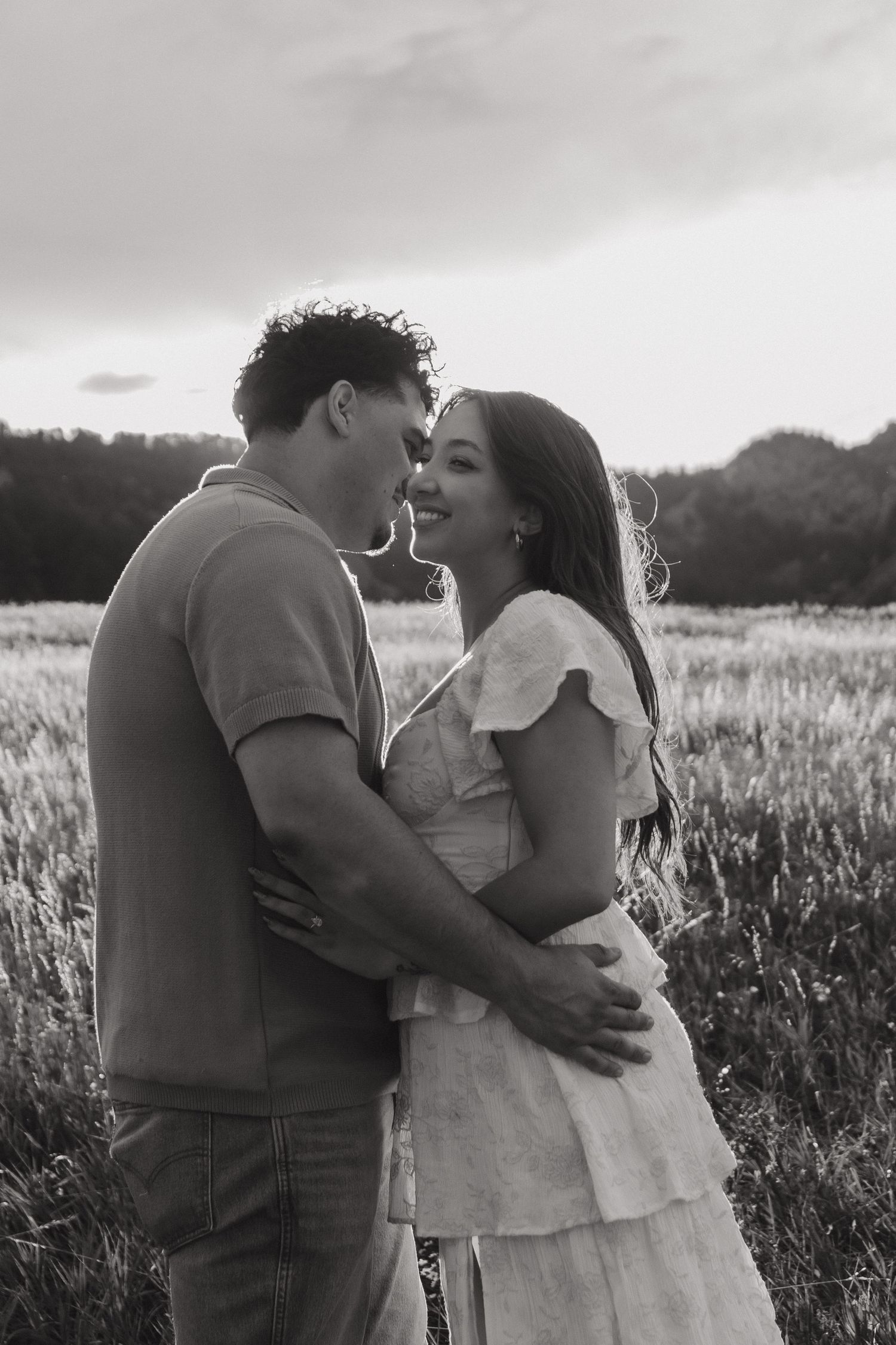 Black and white photo of a smiling couple embracing in a grassy field during an outdoor engagement shoot.
