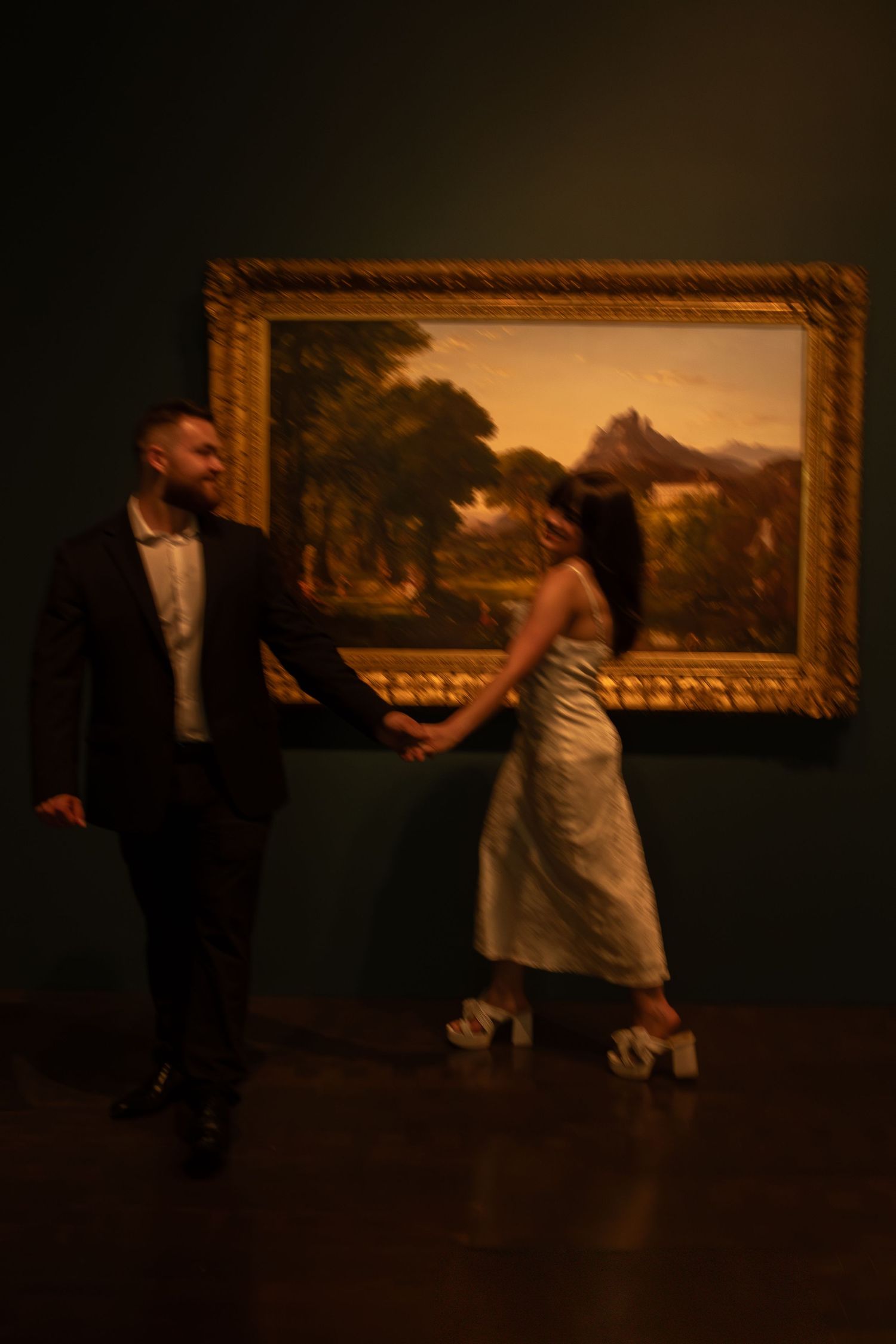 A couple dances together in front of an art gallery wall displaying classical paintings.