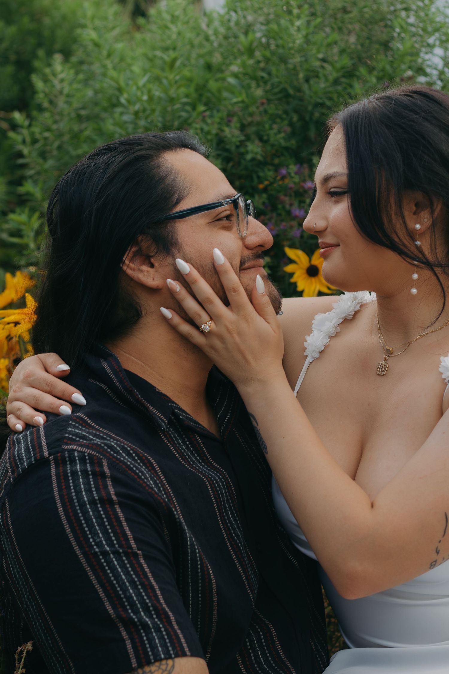 A romantic moment between a couple posing in front of bright yellow sunflowers on a summer day.