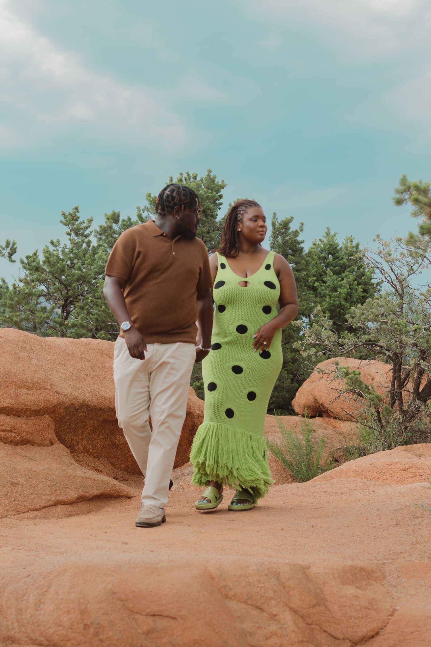 Two people walking together on orange sandstone rock formations under bright blue sky.