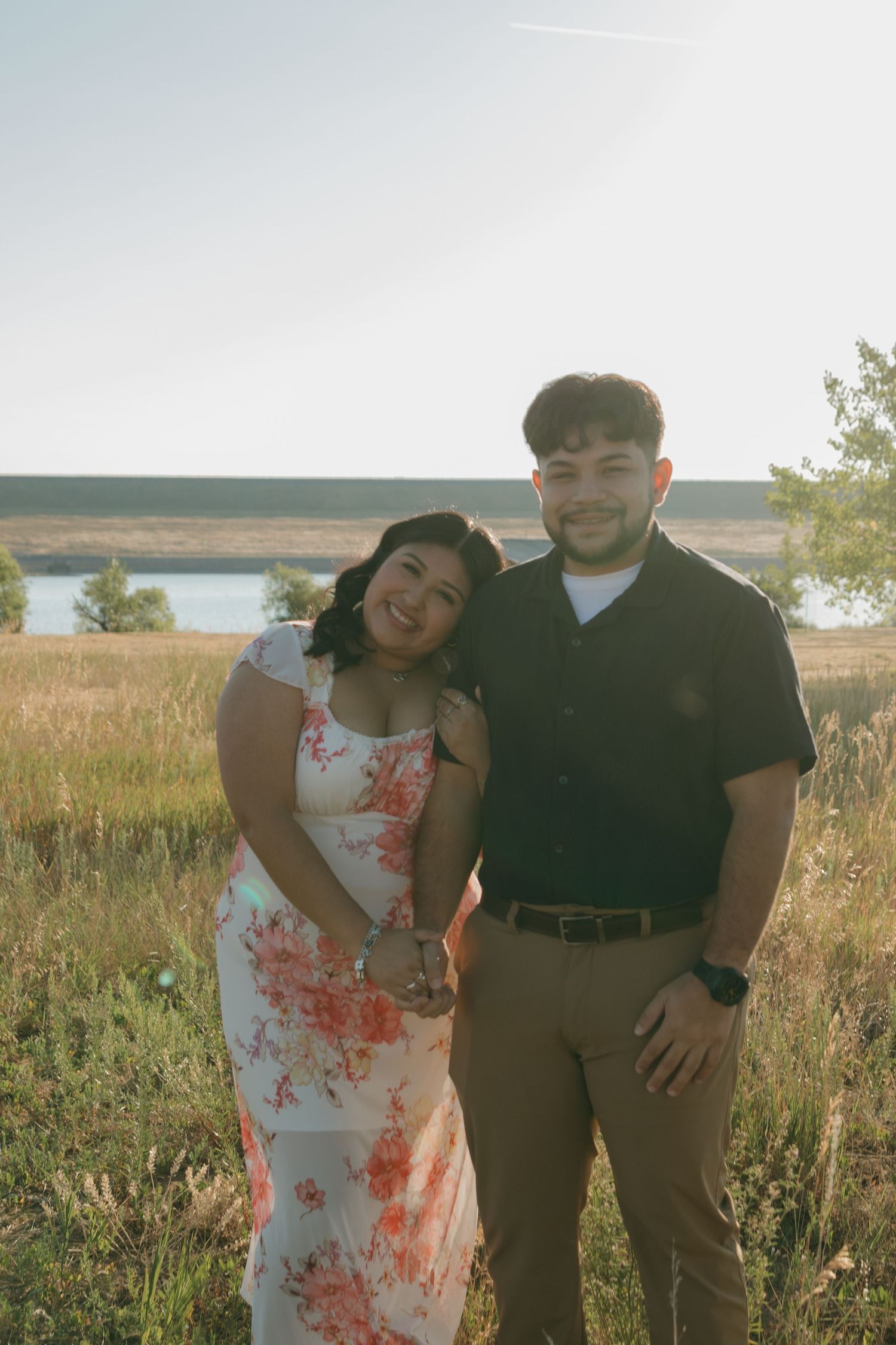 Happy couple posing together in a sun-lit field with mountains in the distance.