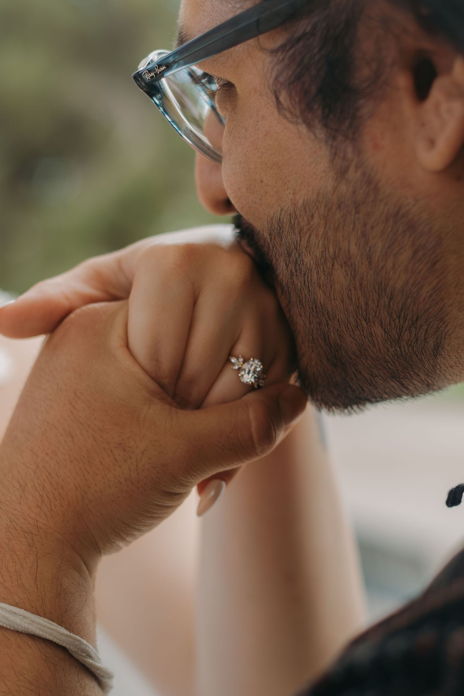 Close-up shot of a person wearing glasses with a diamond ring visible on their hand.