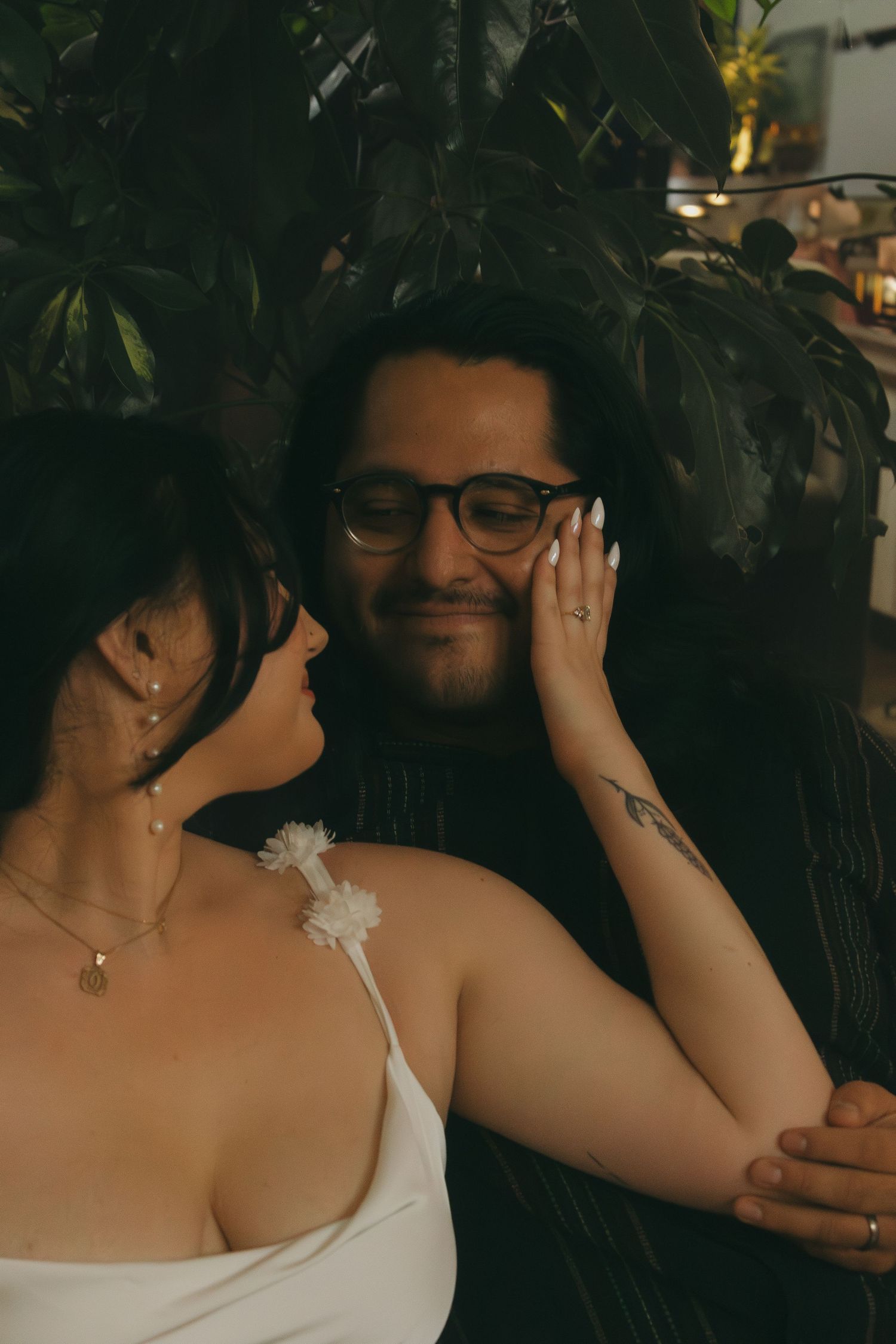 A romantic couple shares a close embrace in front of dark foliage.