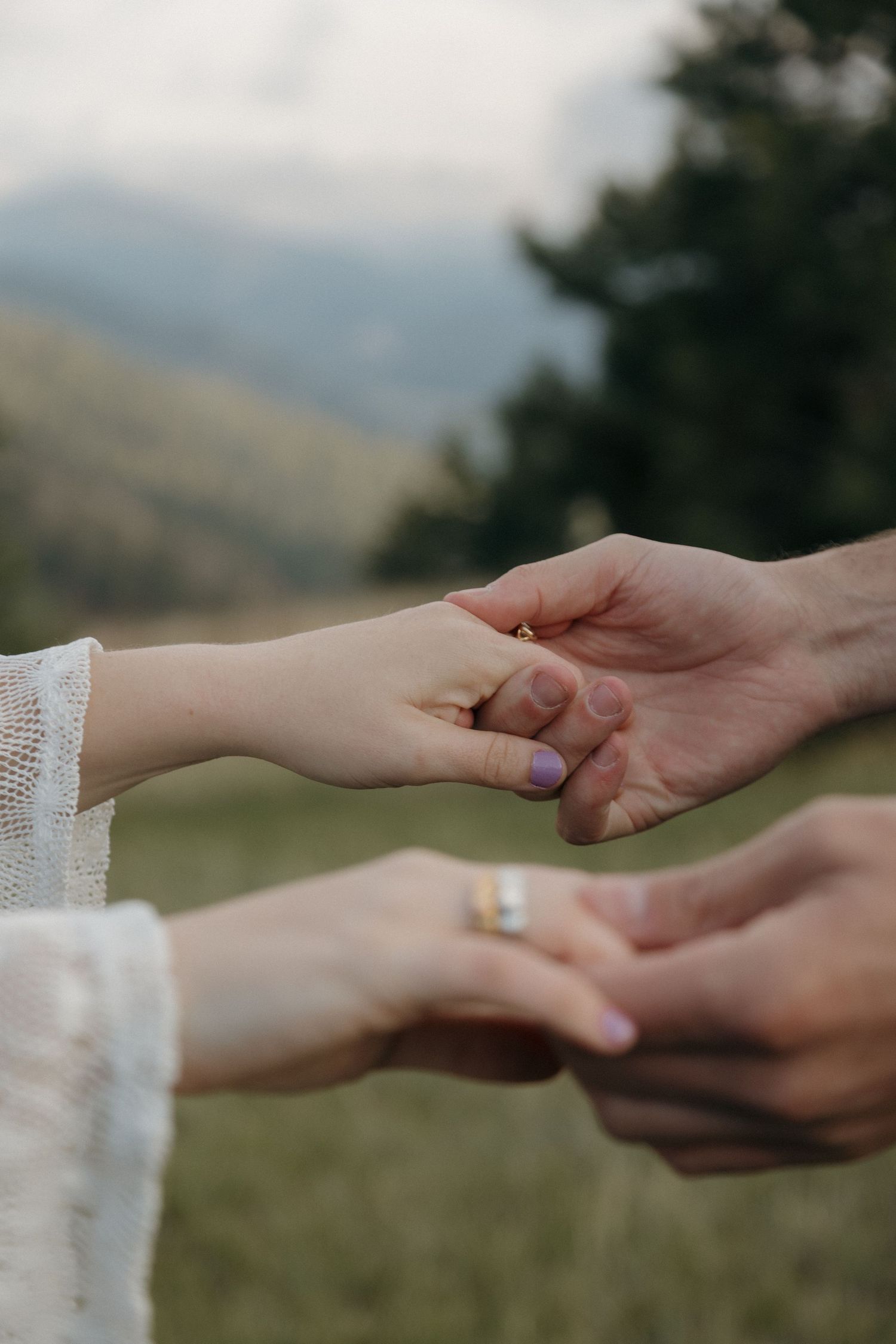 Couple exchanging rings outdoors with mountain backdrop during romantic engagement ceremony.